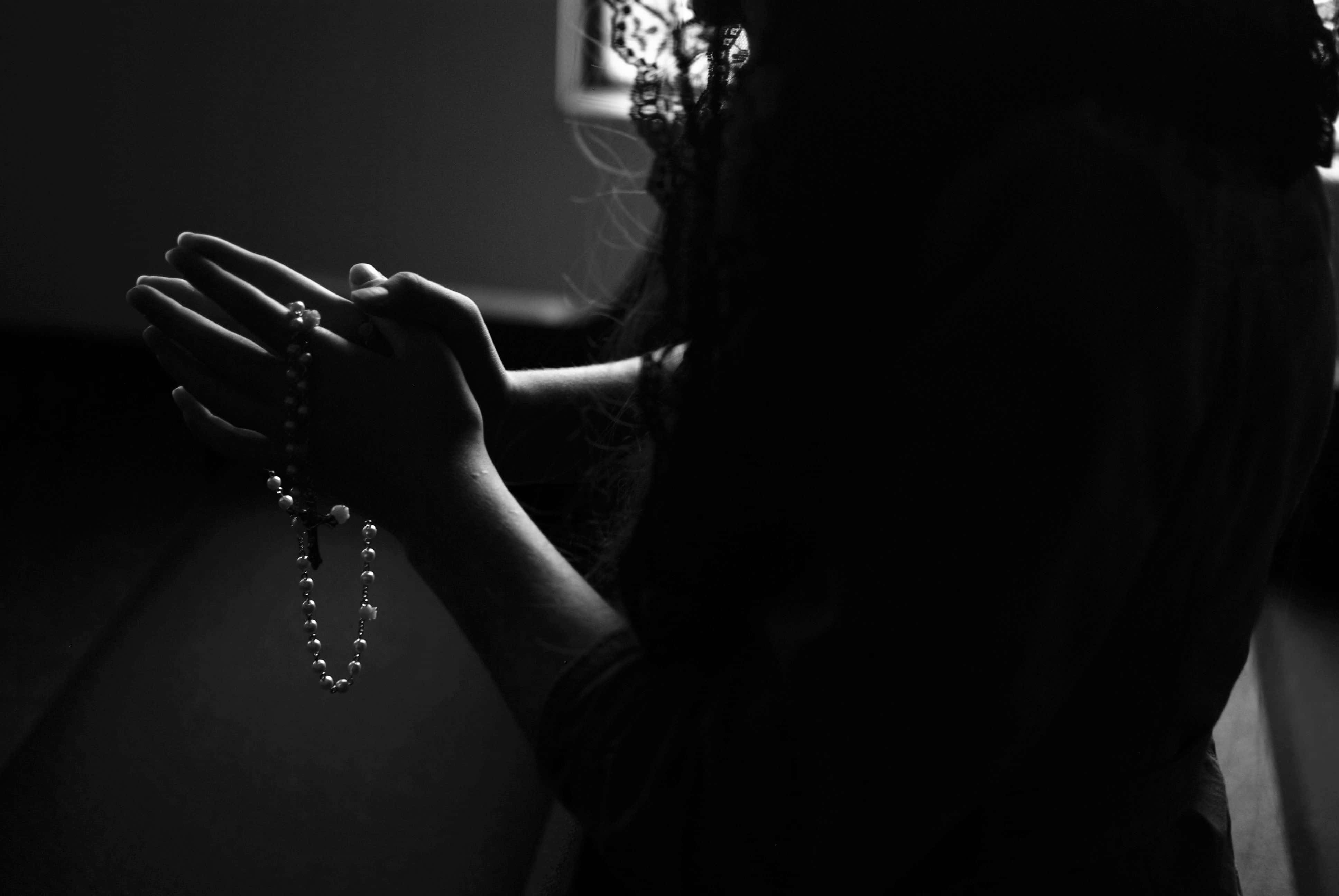 Praying 桌布 壁紙 — 一個剪影中的人雙手合十握著玫瑰經念珠，在柔和背光中祈禱。