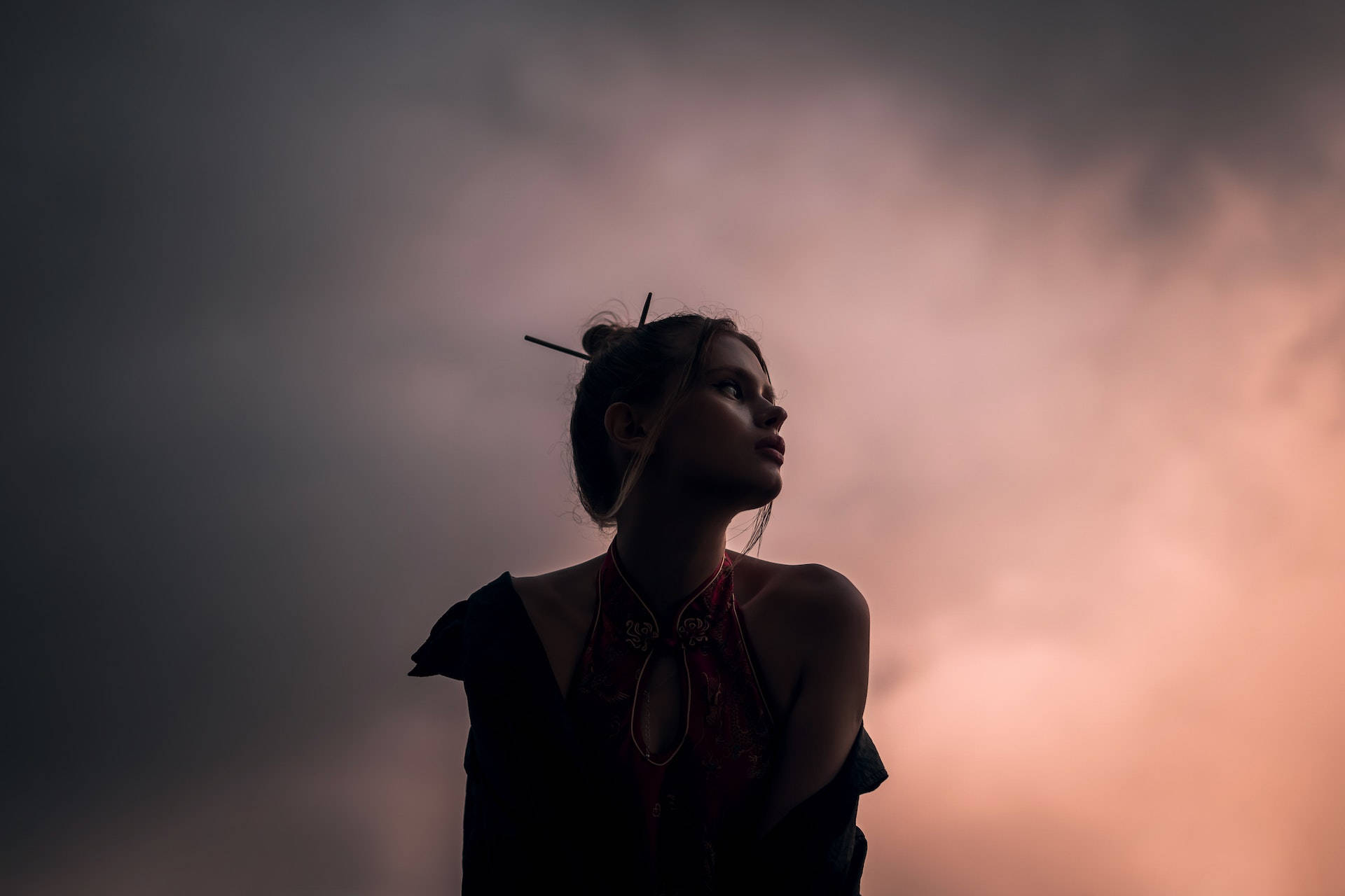 高清 桌布 壁紙 — 一個剪影中的女人仰望戲劇性的黃昏天空，帶有柔和的粉紅色和灰色雲彩。