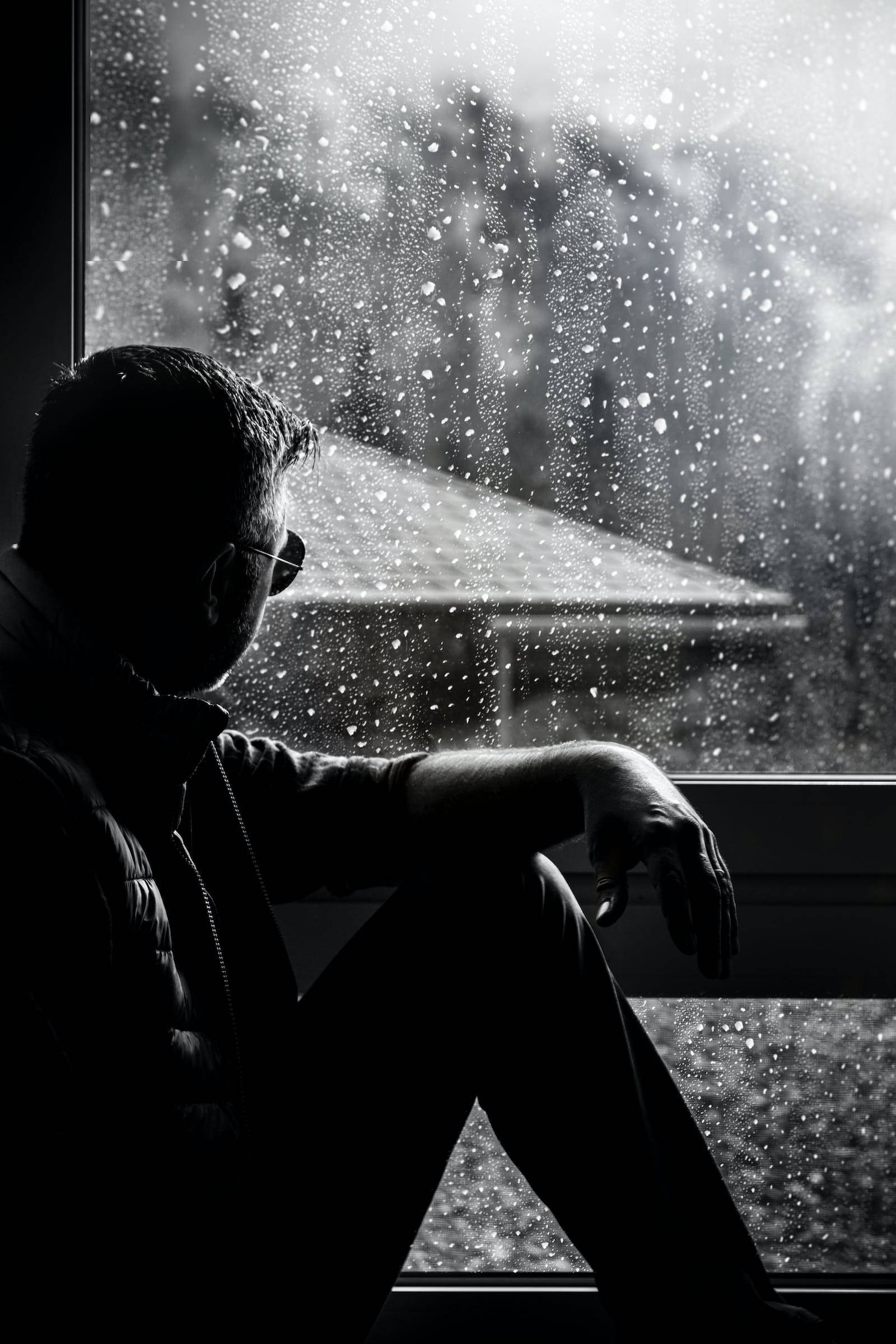 Raining 桌布 壁紙 — 一個剪影中的男人坐在雨點斑駁的窗邊，凝視著單色調中模糊的雪景。