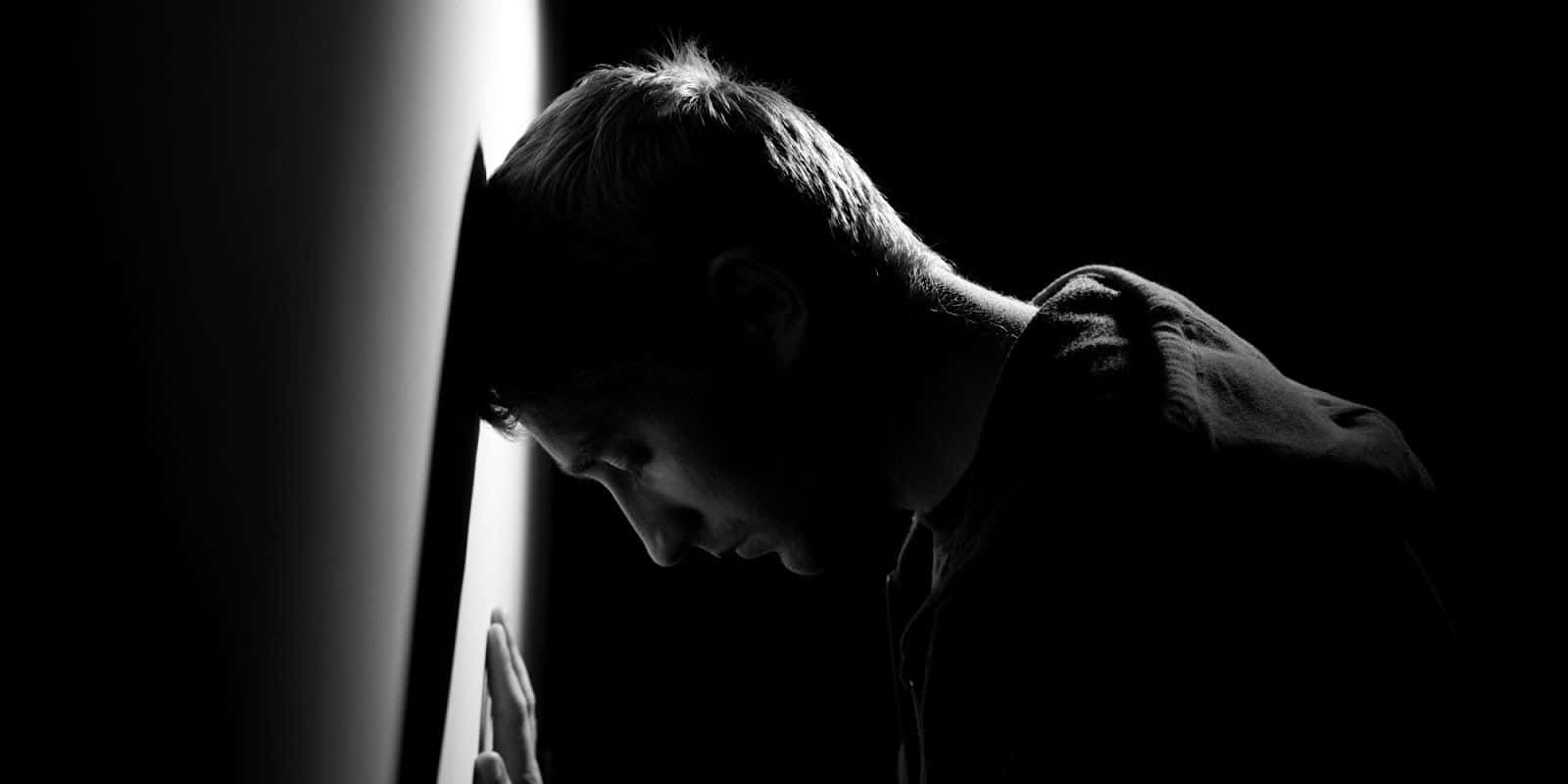 Depressed 桌布 壁紙 — 一個剪影中的男人將頭靠向明亮的垂直光源，構成鮮明的黑白畫面。