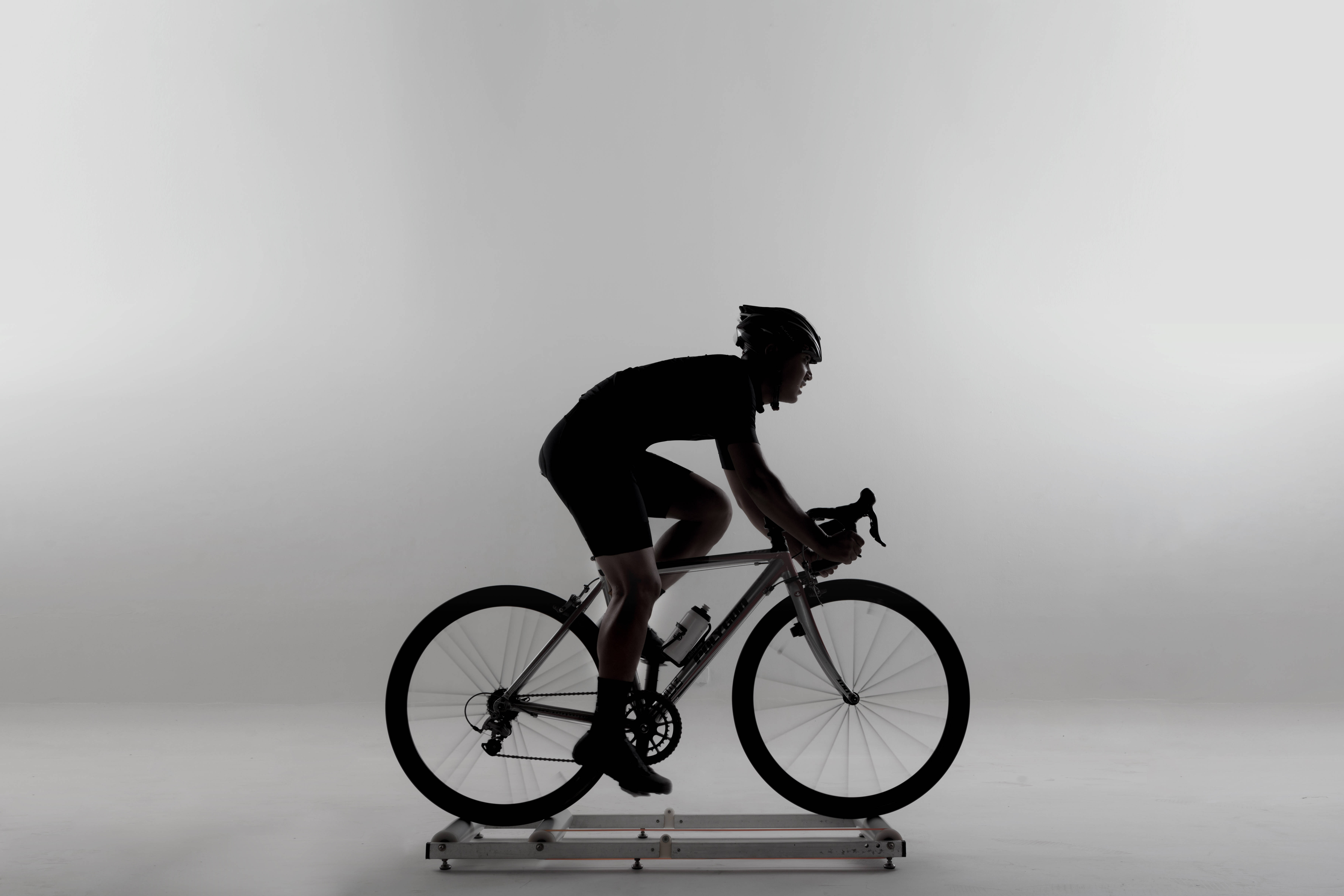 Bicycle 桌布 壁紙 — 一個剪影中的自行車手在純白色工作室背景前，在固定訓練器上激烈踩踏。