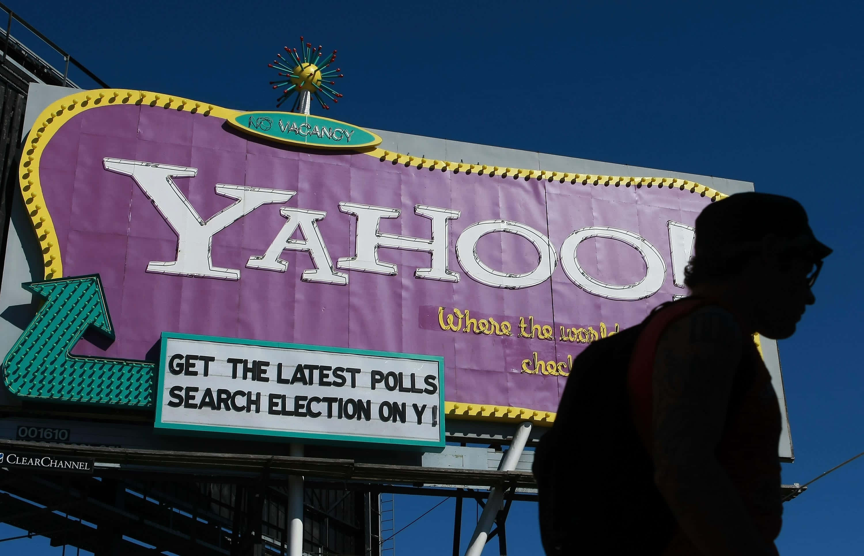 Yahoo 桌布 壁紙 — 一個剪影人物在晴朗的藍天下走過一個大型紫色 Yahoo 廣告看板。