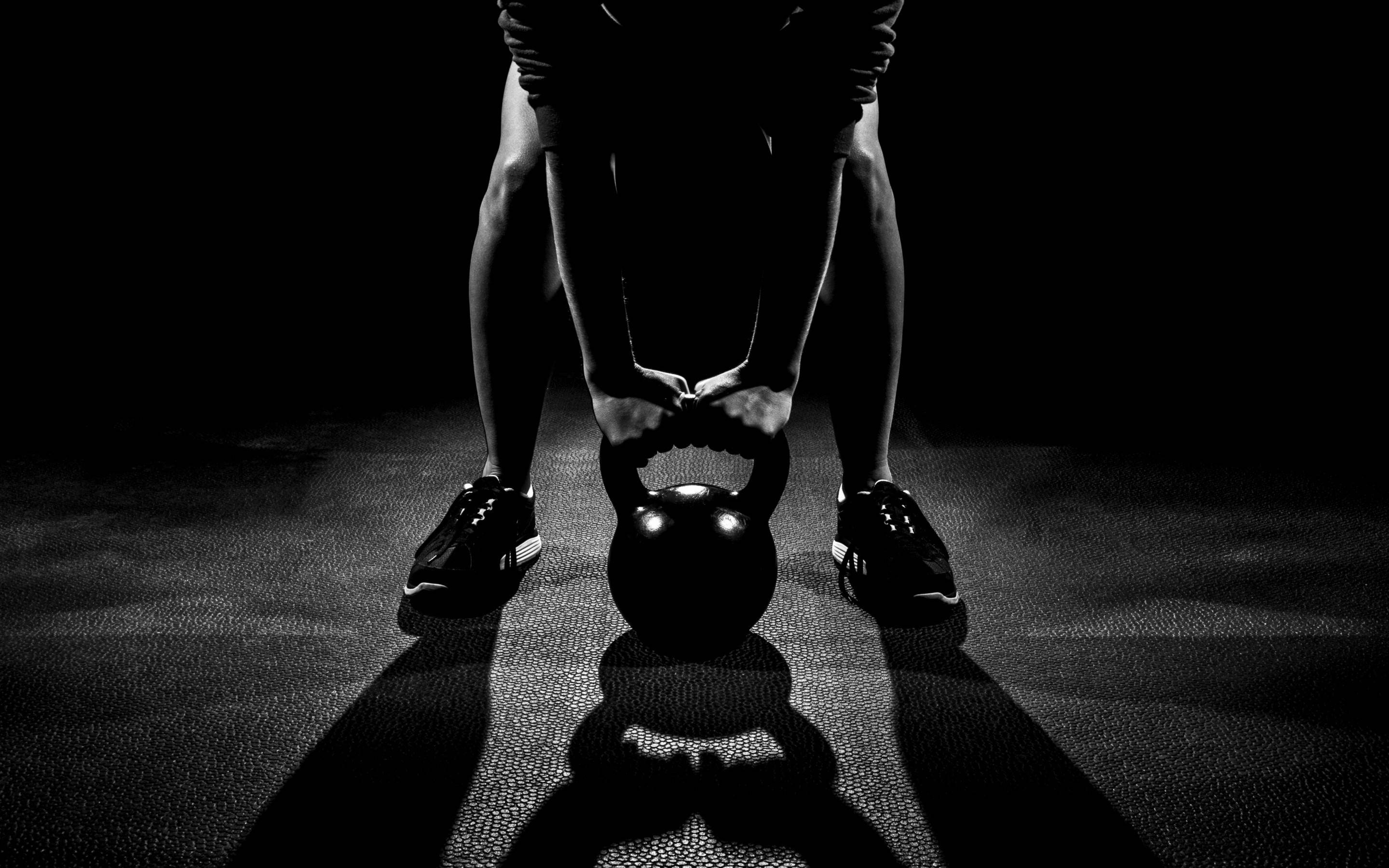 Fitness 桌布 壁紙 — 一個剪影人物在黑暗健身房的戲劇性聚光燈下準備舉起壺鈴。