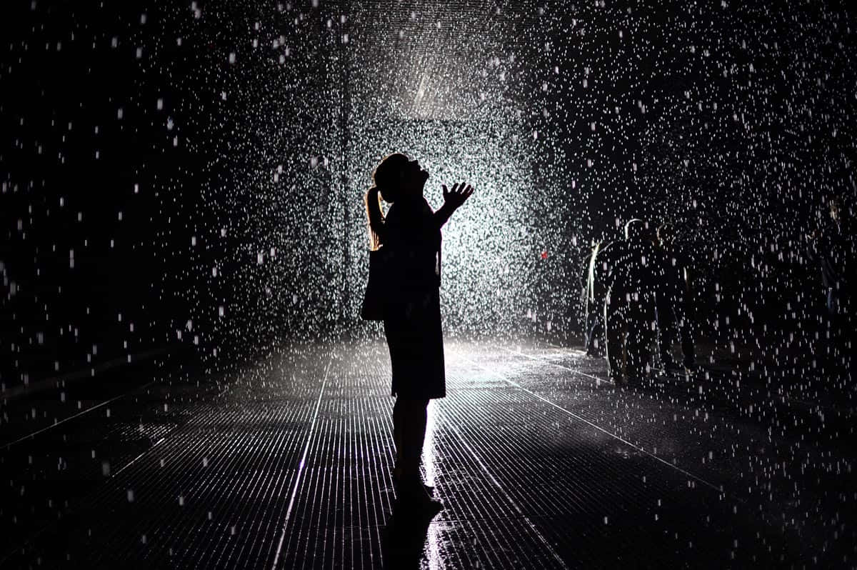 下雨 桌布 壁紙 — 一個剪影人物在黑暗的沉浸式藝術裝置中，舉起雙臂站在落下的水滴下。