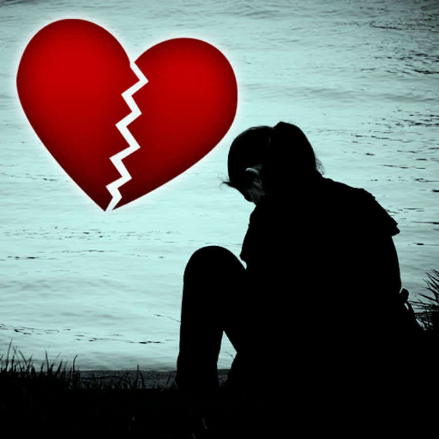 Broken Heart Sad 桌布 壁紙 — 一個剪影人物坐在水邊，一個發光的紅色破碎心臟懸浮在他們上方。