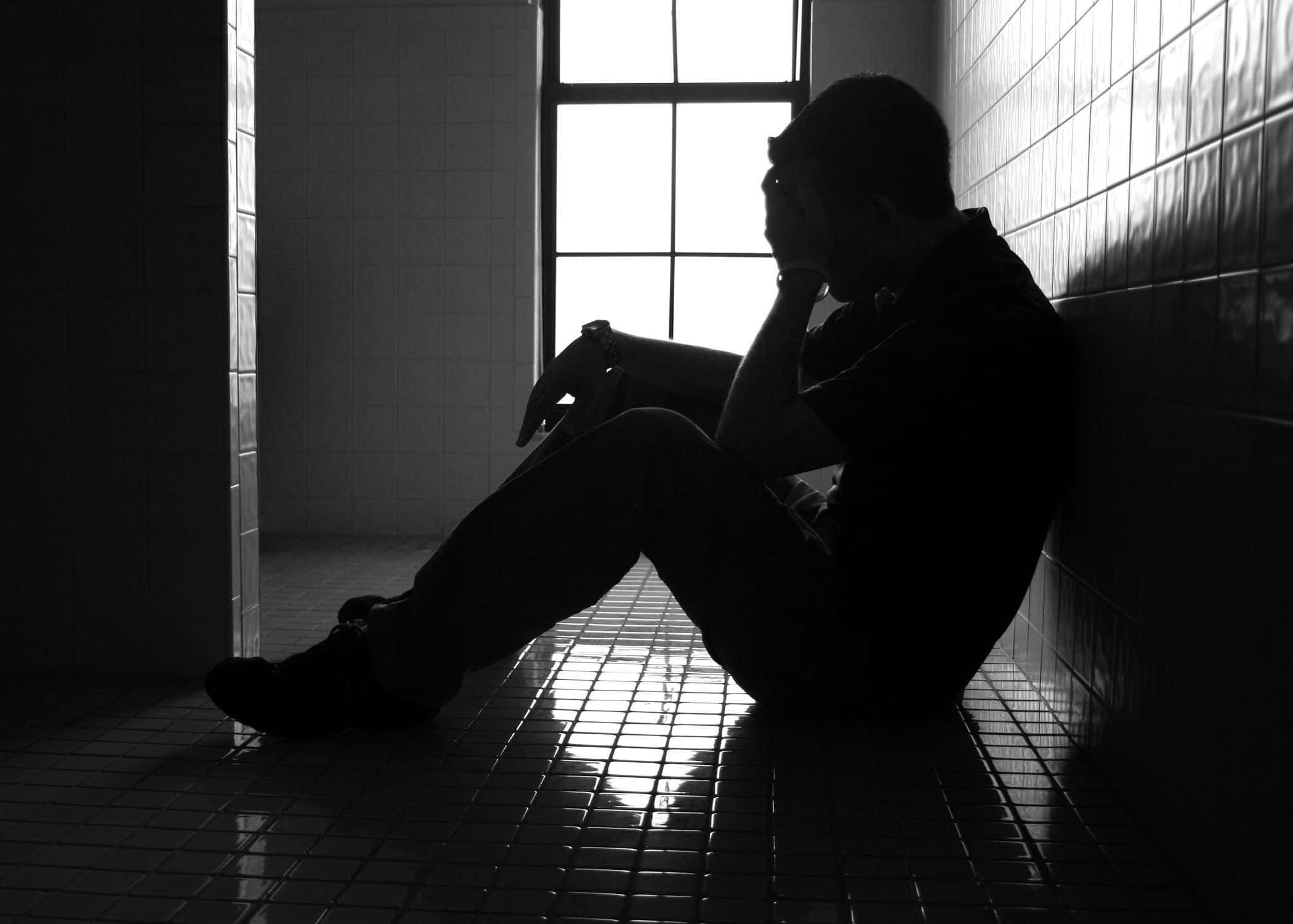 Sad Face 桌布 壁紙 — 一個剪影人物獨自坐在鋪滿瓷磚的房間裡，雙手抱頭，沐浴在窗戶射進來的強光中。