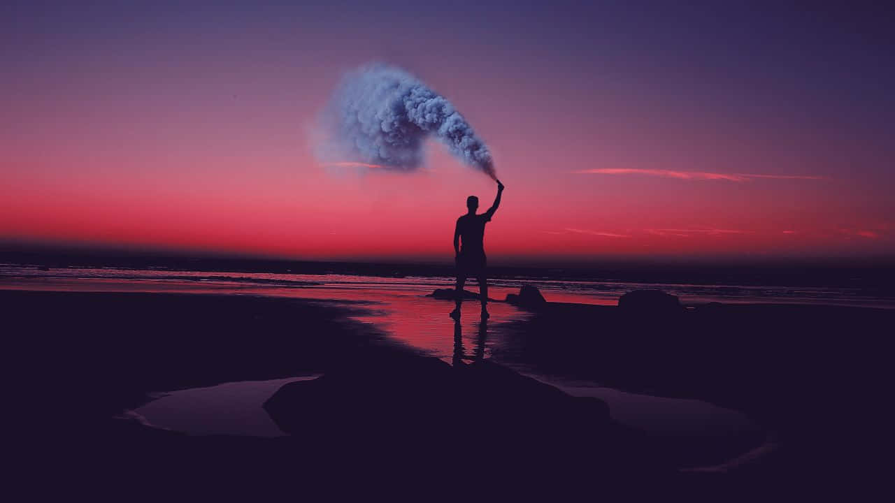 dreams 桌布 壁紙 — 一個剪影人物站在日落時分的濕沙灘上，手持一支信號彈，向著充滿活力的粉紅和紫色天空釋放出一縷煙霧。