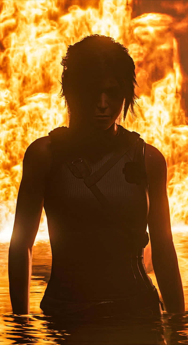 iPhone Xs Rise Of The Tomb Raider 桌布 壁紙 — 一個剪影人物站在水深及腰的位置，背景是咆哮的橙色火焰。