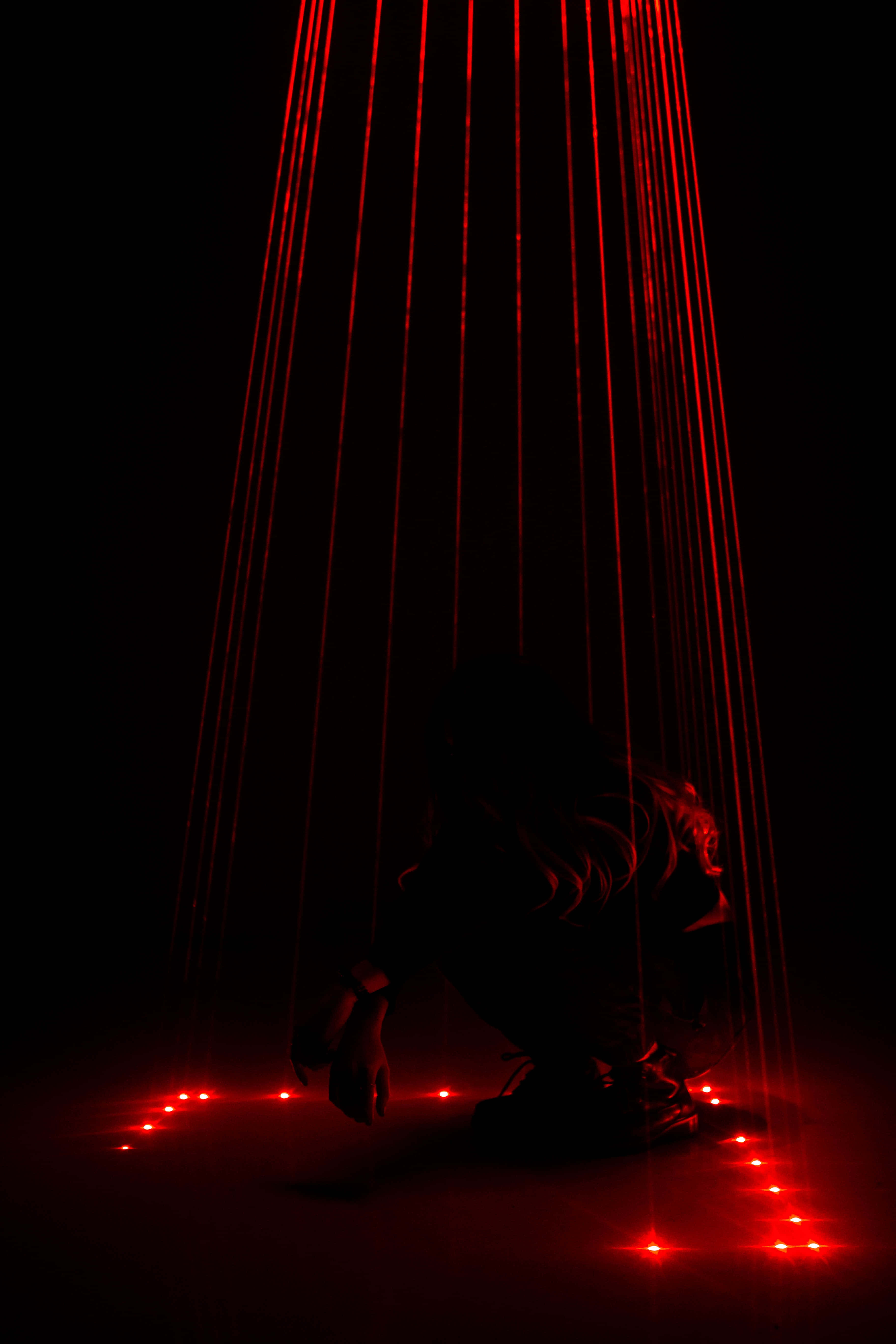Laser 桌布 壁紙 — 一個剪影人物蹲在層疊的紅色雷射光束下，身處漆黑虛空，地板上有發光的紅點。