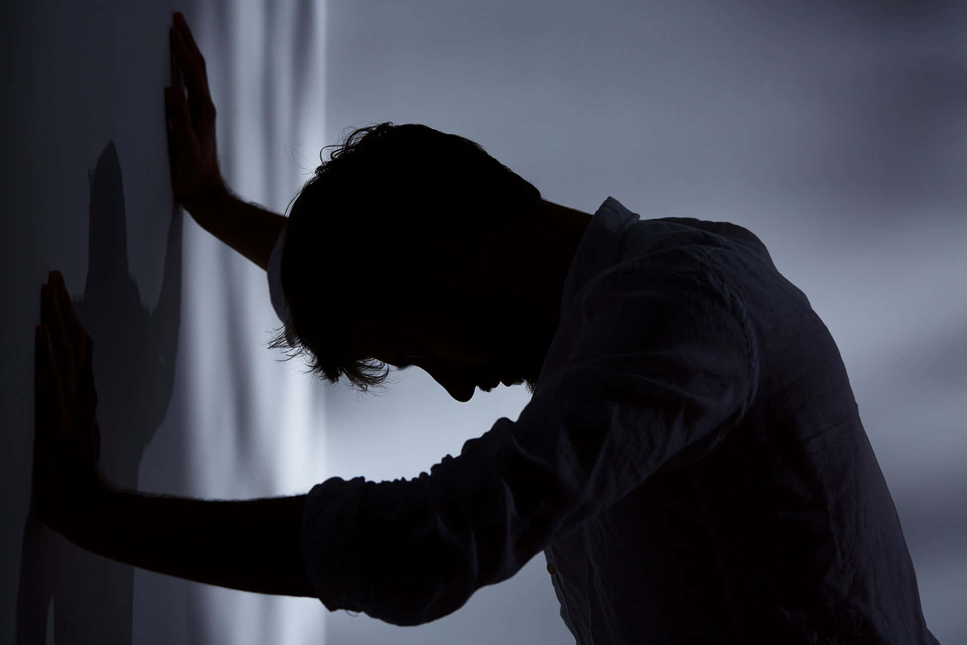 Depressed 桌布 壁紙 — 一個剪影人物靠著牆壁，雙手按在表面，在昏暗的房間裡。