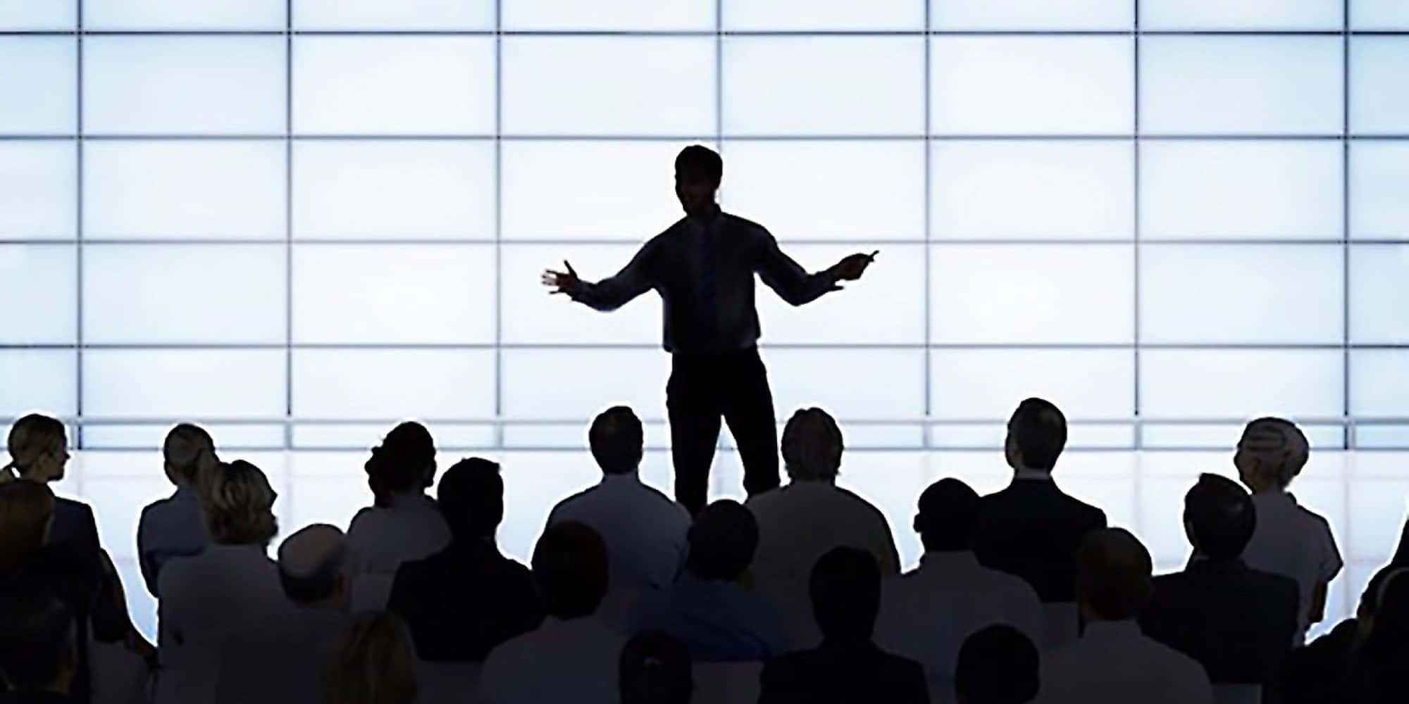 Leadership 桌布 壁紙 — 一個剪影演講者向坐在明亮網格牆前的觀眾做出廣泛的手勢。