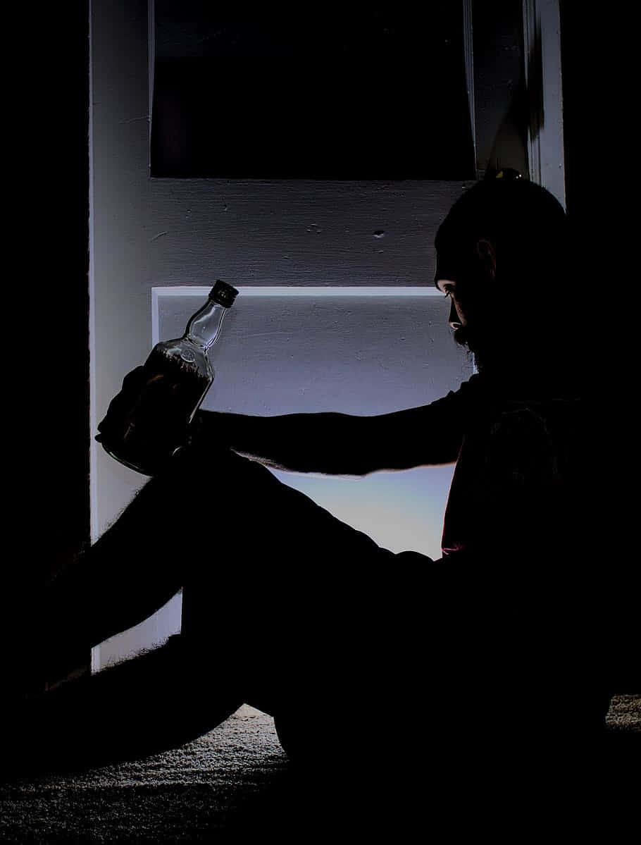 Drinking 桌布 壁紙 — 一個剪影男子坐在黑暗中手持瓶子，被背後一道狹窄的光束照亮。