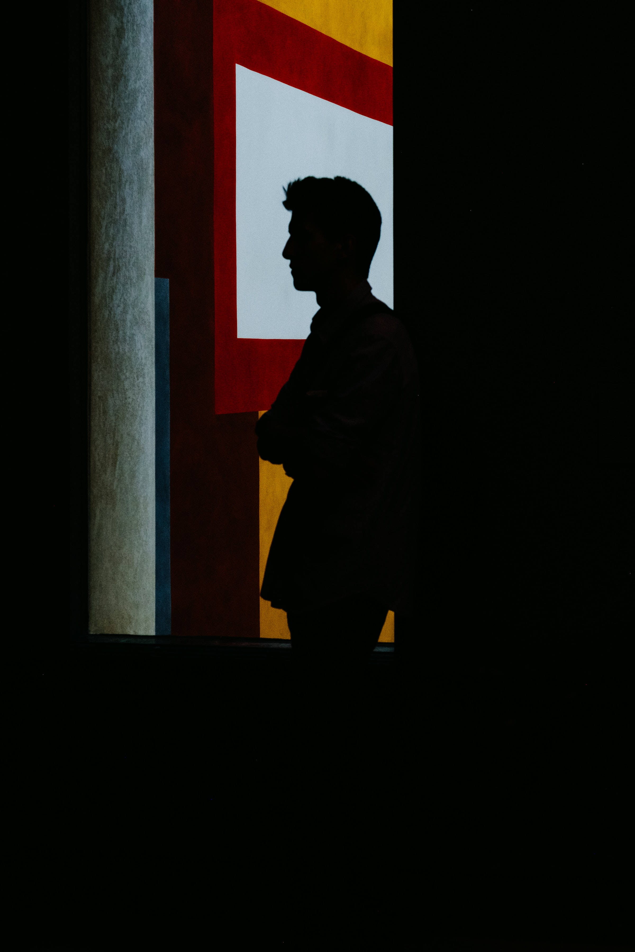 Silhouette 桌布 壁紙 — 一個剪影男子站在黑暗中，旁邊是一個明亮照明的抽象幾何窗戶，帶有紅色、黃色和白色面板。
