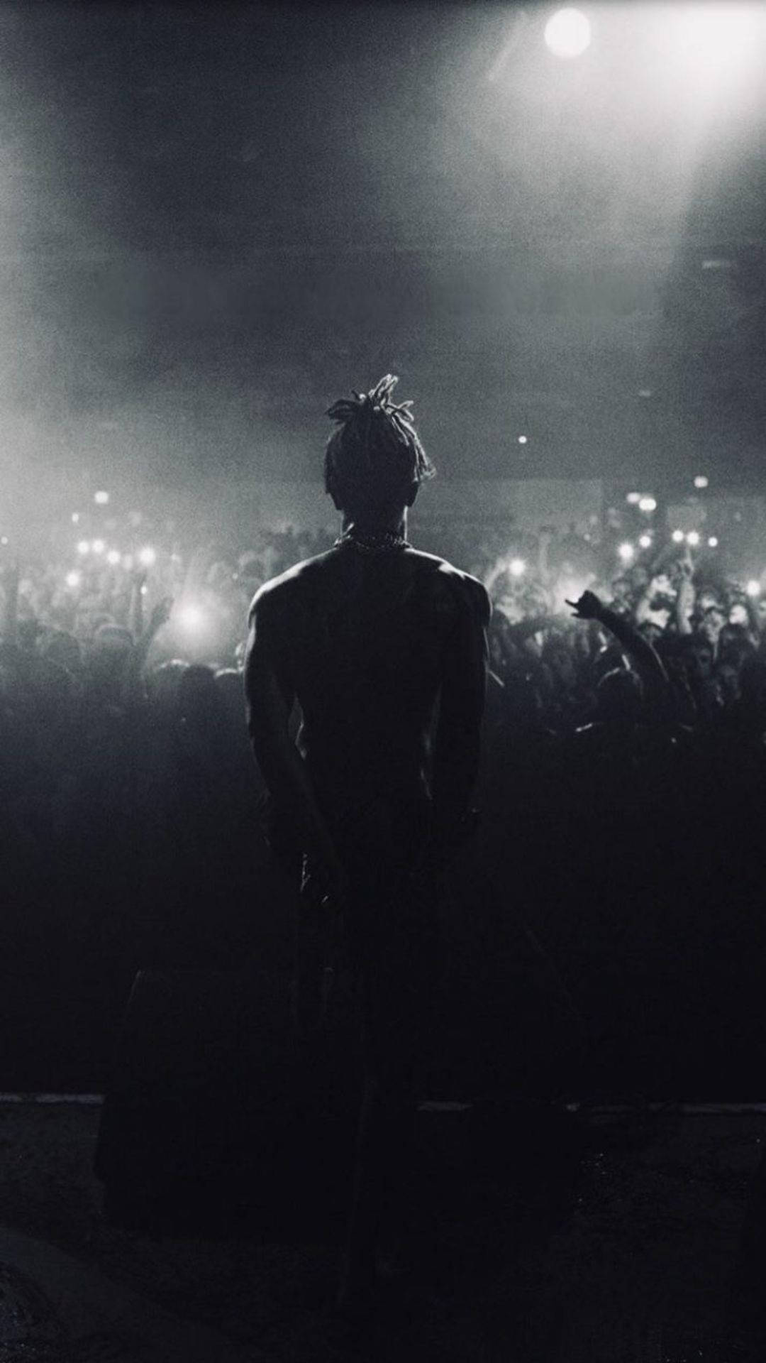 酷酷的xxxtentacion 桌布 壁紙 — 一個剪影表演者站在舞台上，在聚光燈下，面對著音樂會中高舉手機的熱情人群。