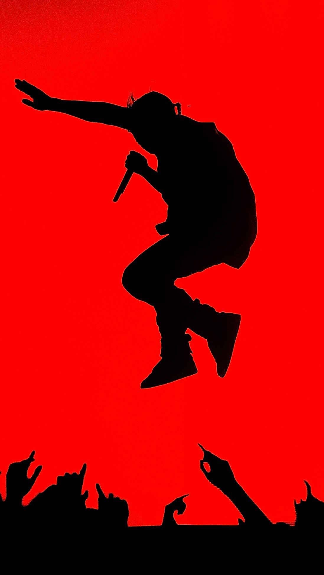 Kanye 桌布 壁紙 — 一個動態剪影，一位饒舌歌手在半空中手持麥克風，背景是鮮豔的紅色，下方有群眾的手向上伸展。