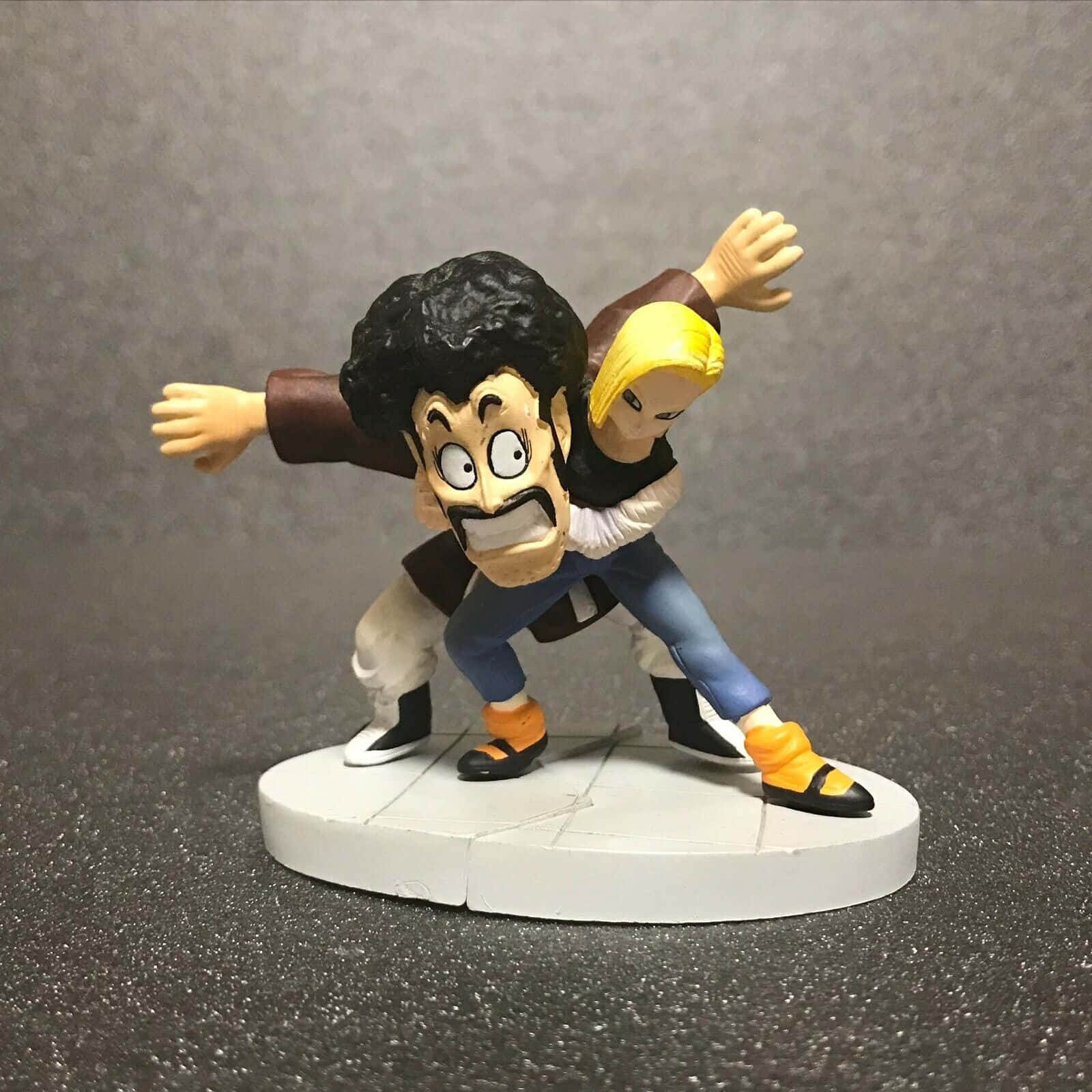 Hercule Satan 桌布 壁紙 — 一個動態動漫動作人偶描繪了一個肌肉發達、黑髮留鬍的男人與一個金髮女人在緊張的戰鬥姿勢中搏鬥。