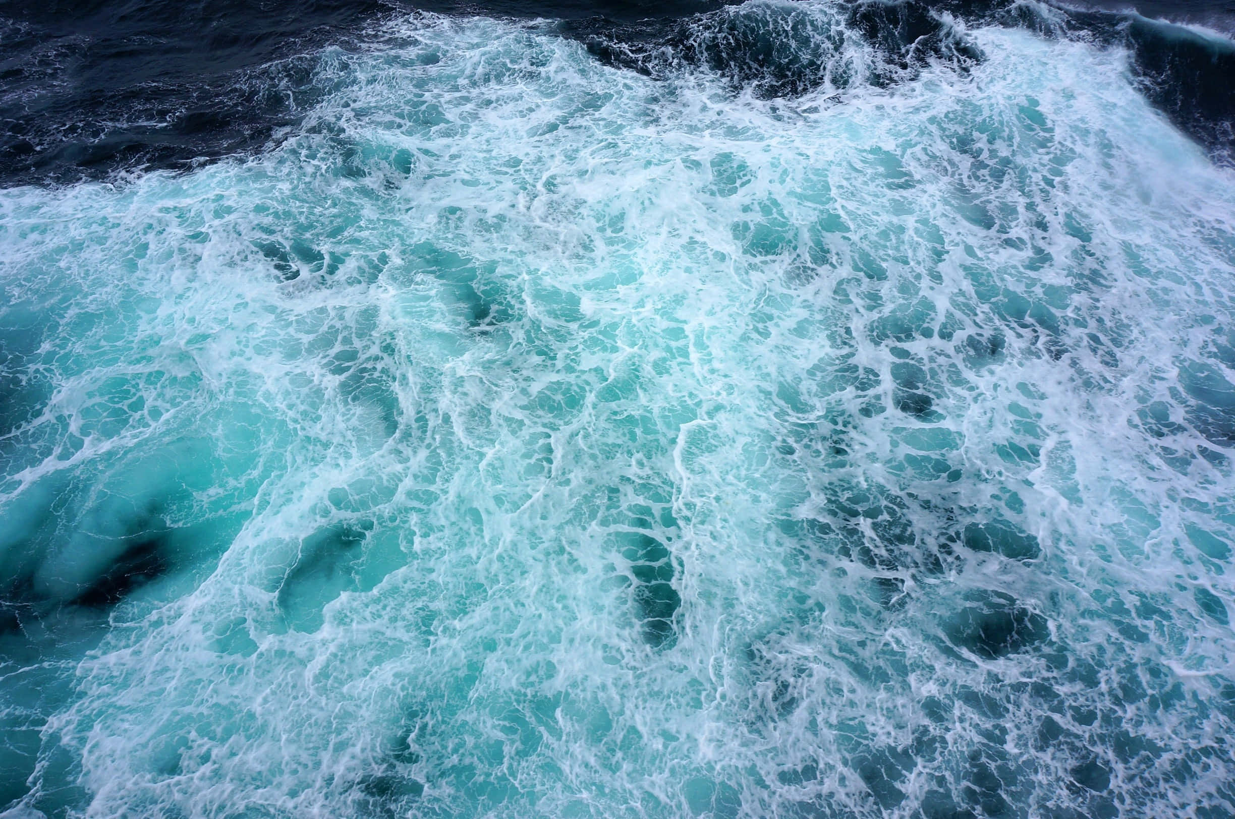 Ocean Water 桌布 壁紙 — 一個動態特寫，呈現綠松石色的海浪拍打並泛起白色浪花，與深色海水形成對比。