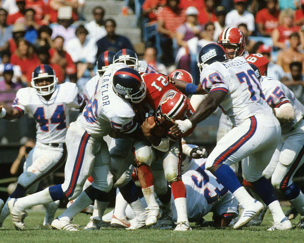 足球 桌布 壁紙 — 一個動態的1980年代NFL美式足球比賽畫面，顯示身穿白色和紅色球衣的球員在陽光明媚的球場上擒抱持球者。