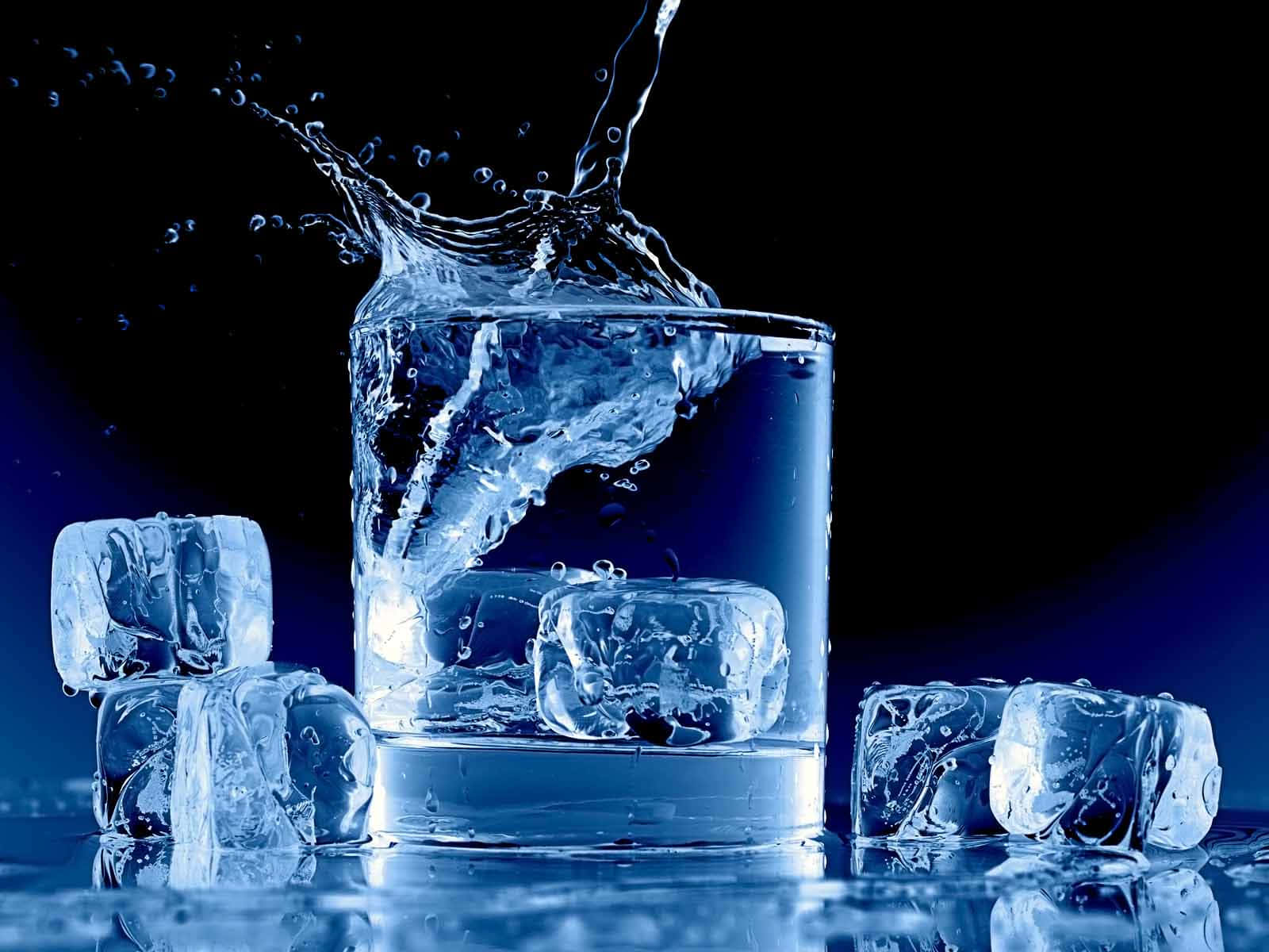 Splash 桌布 壁紙 — 一個動態的水花從裝滿冰塊的玻璃杯中噴出，背景是深藍色。