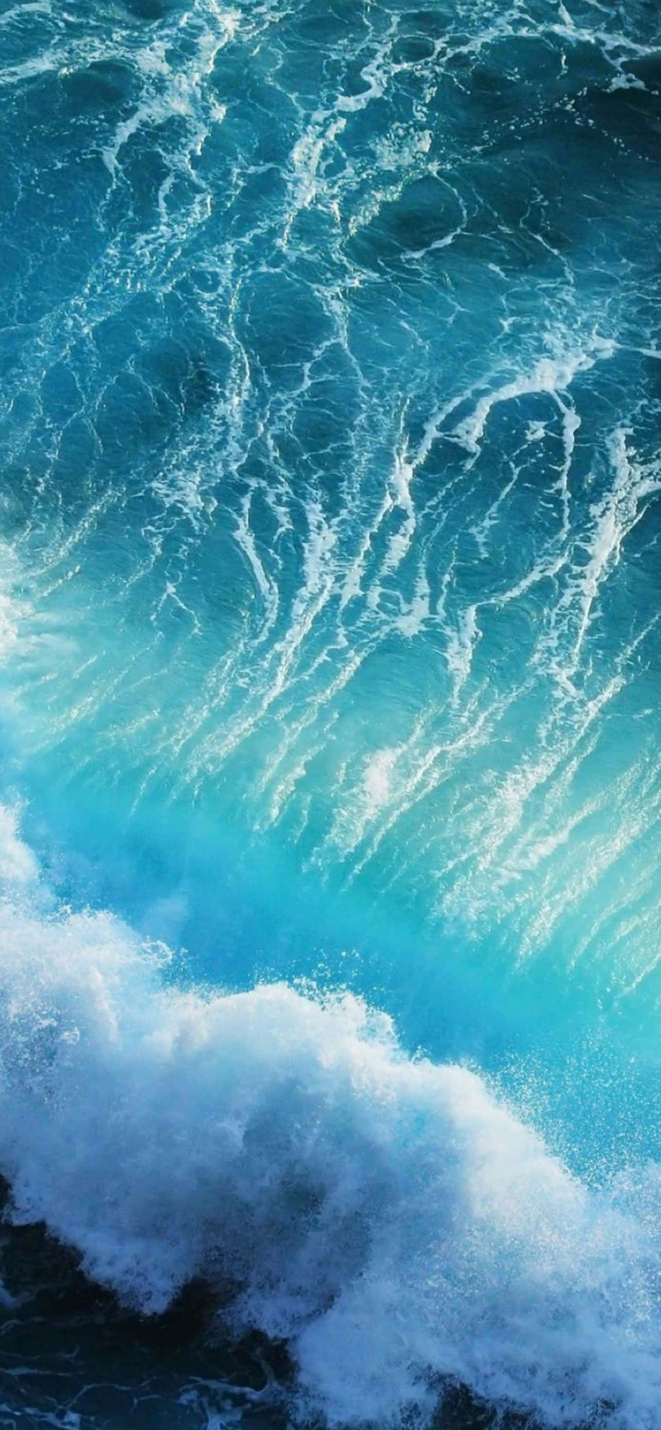 Blue iPhone 桌布 壁紙 — 一個動態的特寫，呈現藍綠色海浪拍打著深藍色大海，激起白色泡沫。