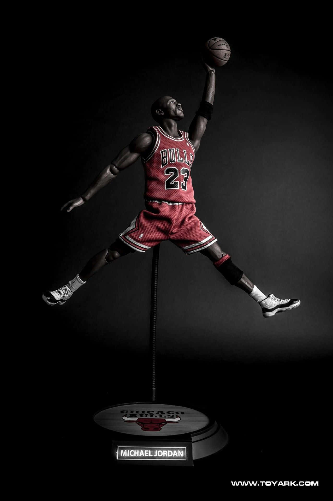 Jordan Logo Phone 桌布 壁紙 — 一個動態雕像，麥可喬丹在半空中灌籃，身穿標誌性的紅色芝加哥公牛隊球衣，背景是深色攝影棚。