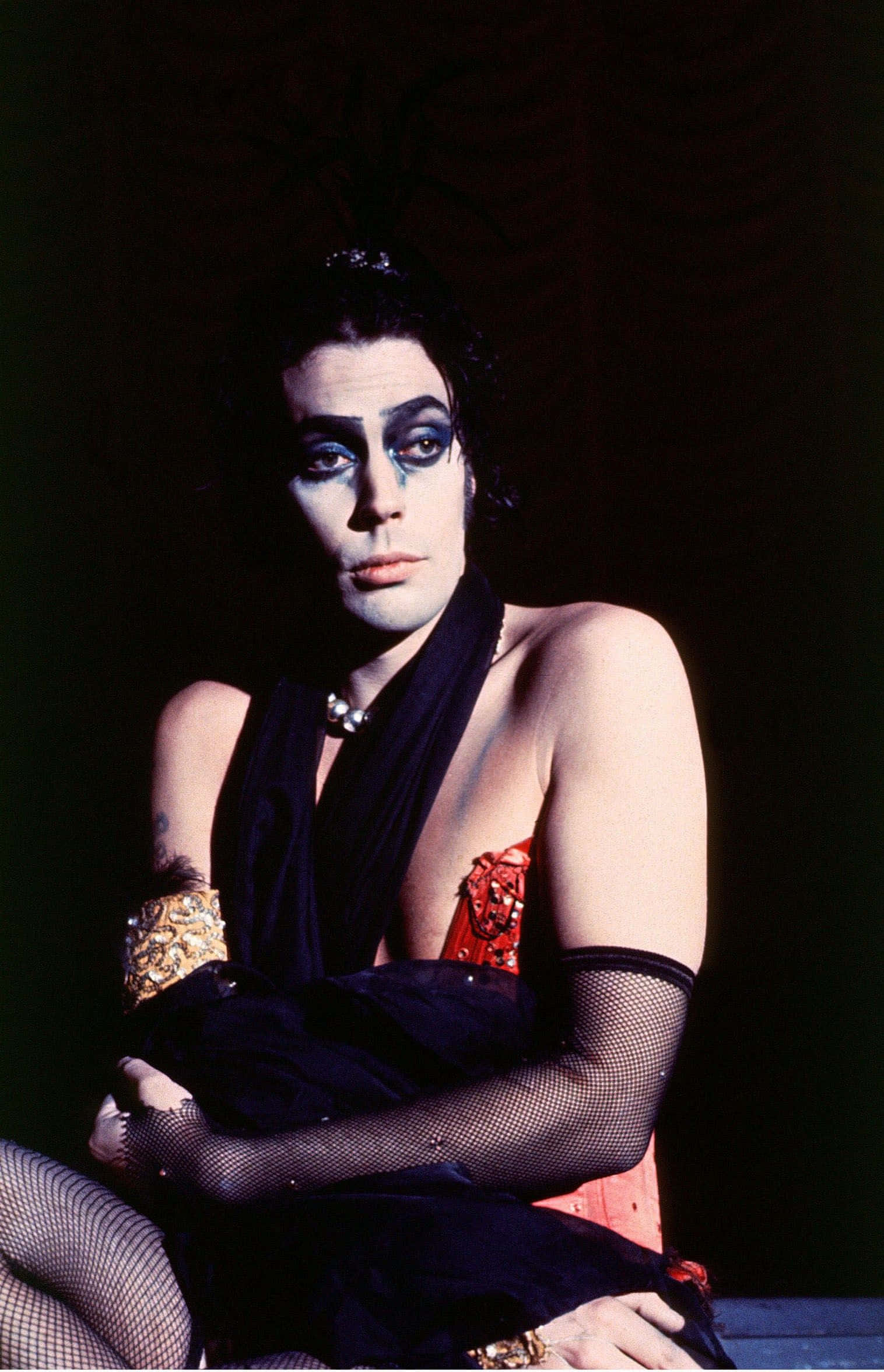 Tim Curry 桌布 壁紙 — 一個化著戲劇性藍色眼妝、身穿黑色漁網服裝的人，在黑暗背景前擺姿勢。