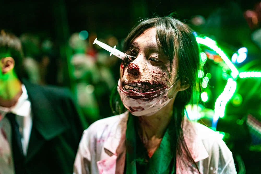 Scary Zombie 桌布 壁紙 — 一個化著殭屍妝的人，眼睛插著注射器，站在恐怖活動的霓虹綠燈下。