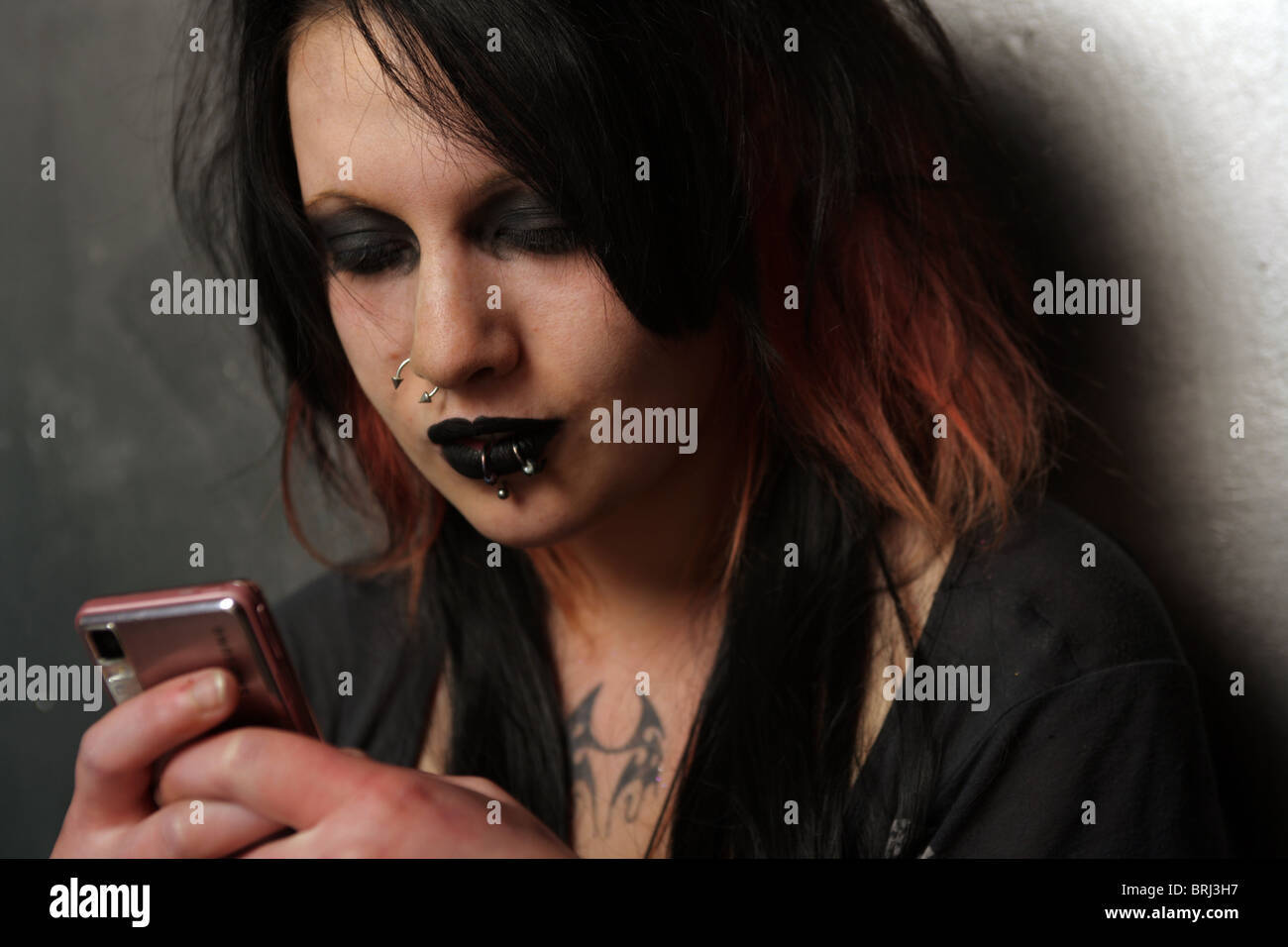Gothic Phone 桌布 壁紙 — 一個化著深色妝容、髮尾染紅的人靠在牆上，專注地用粉紅色手機發簡訊。