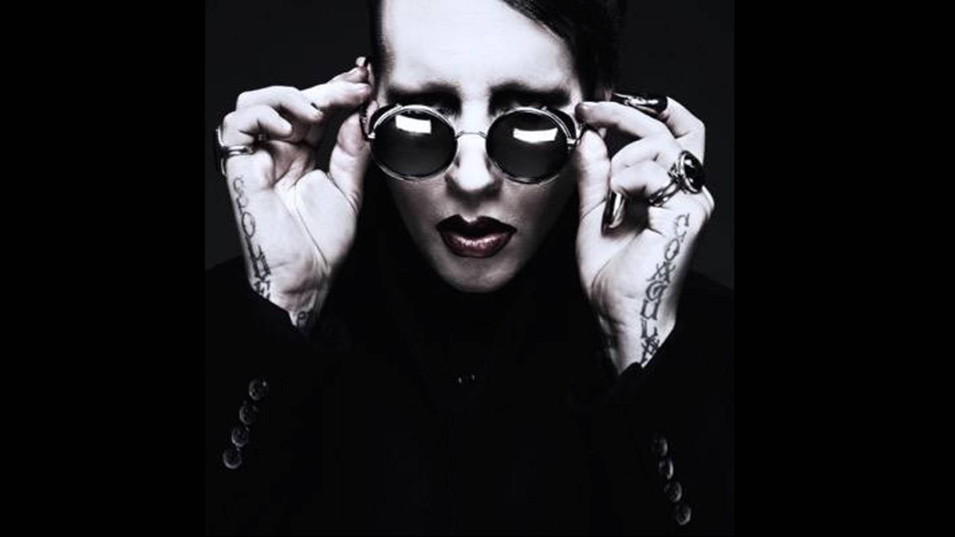 Sunglasses 桌布 壁紙 — 一個化著濃妝、有刺青的人，在黑色背景前調整圓形太陽眼鏡。