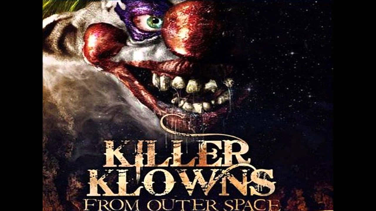 killer klowns from outer space 桌布 壁紙 — 一個化著紫色妝容、牙齒沾滿鮮血的怪誕外星小丑，從星夜中的宇宙煙霧中浮現。