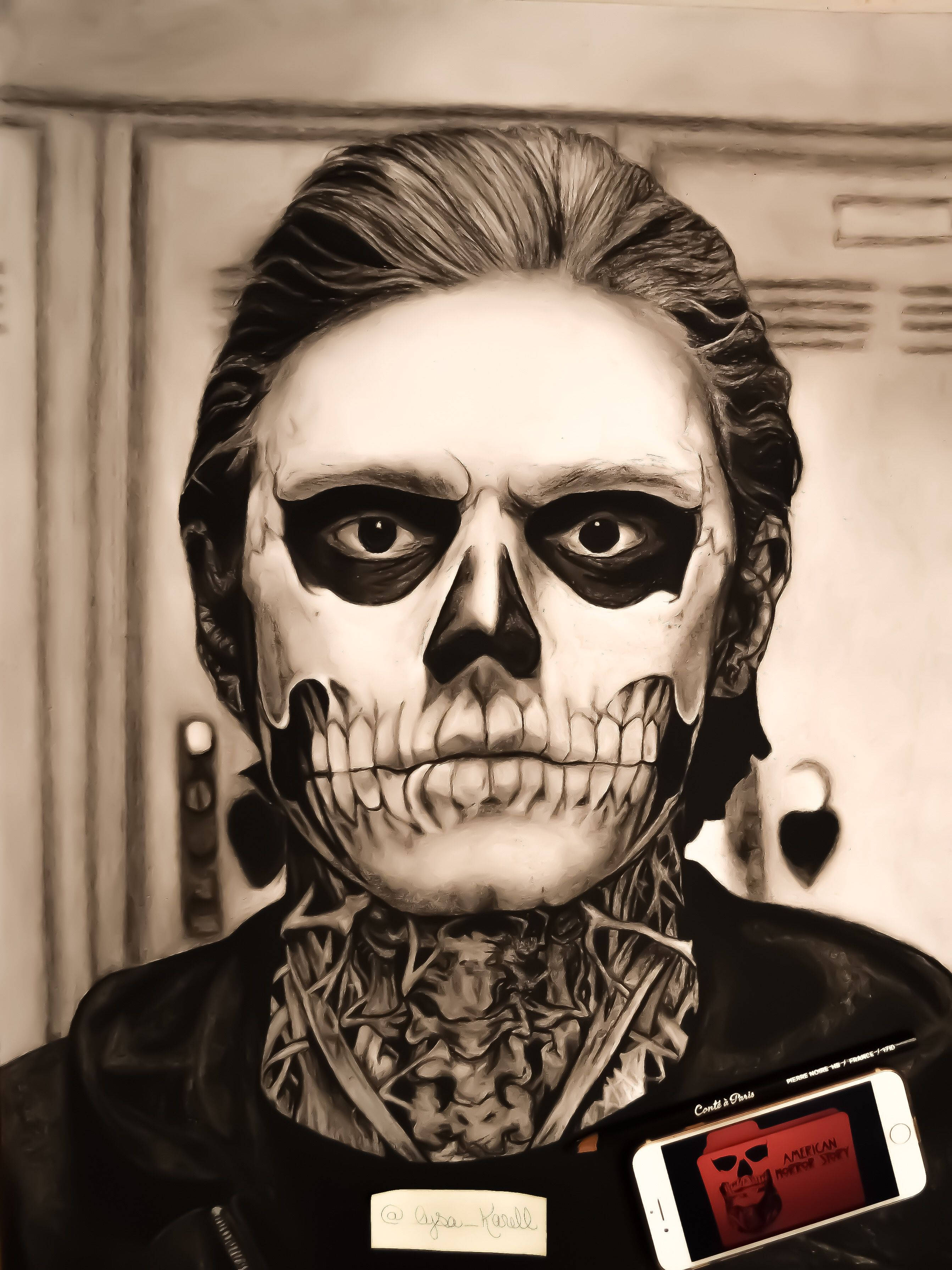 Tate Langdon 桌布 壁紙 — 一個化著骷髏妝容和紋身的人，在更衣室裡拿著顯示骷髏圖案的手機，眼神銳利。