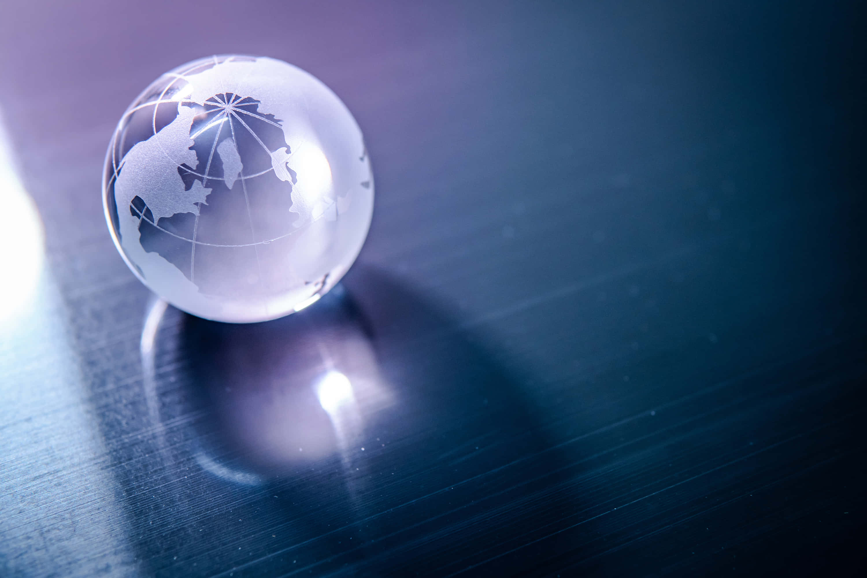 World 桌布 壁紙 — 一個半透明玻璃地球儀，上面蝕刻著大陸，放置在深色反光表面上，在冷藍色燈光下。