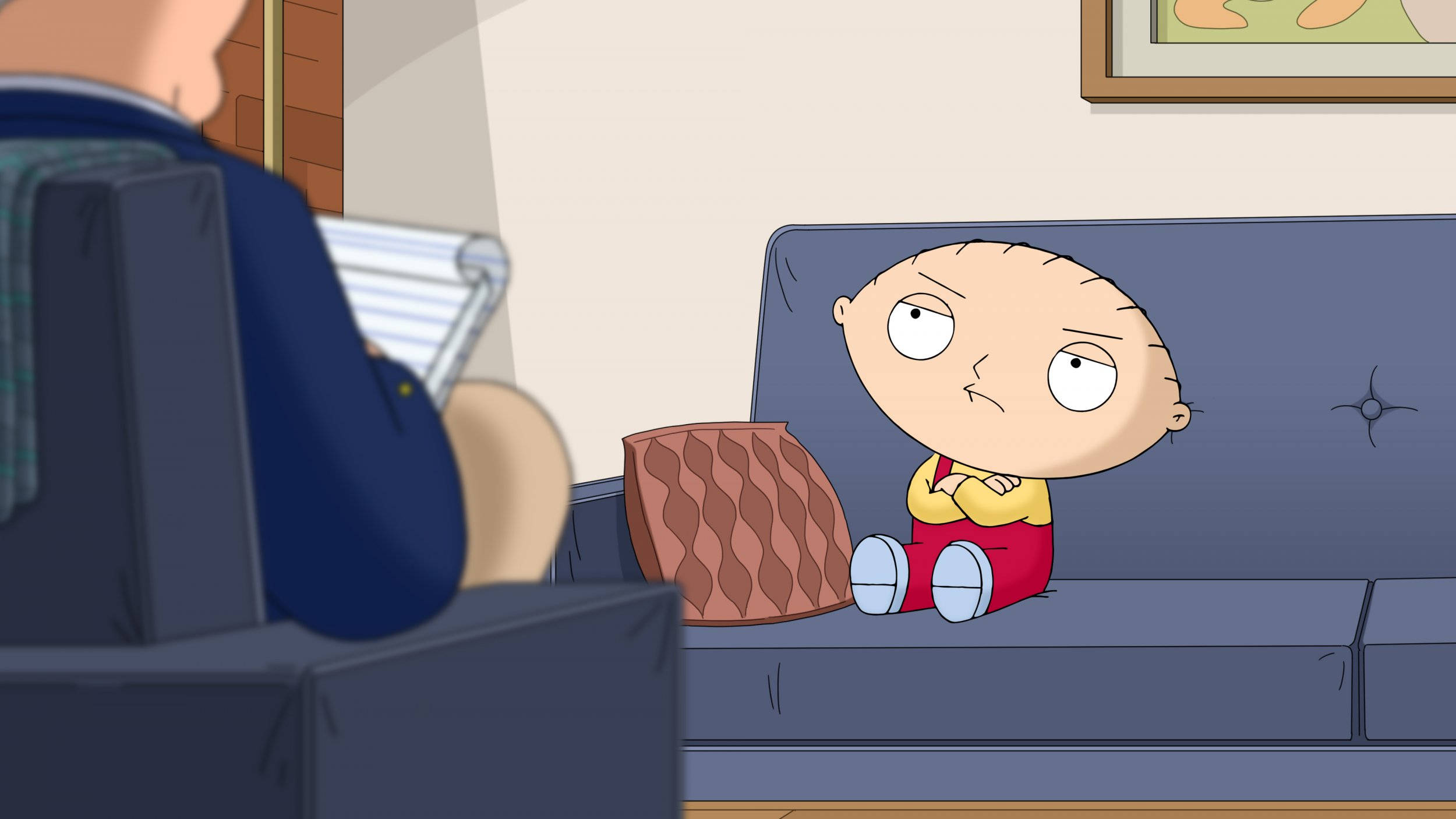 stewie 桌布 壁紙 — 一個卡通嬰兒皺著眉頭坐在藍色沙發上，旁邊有一個圖案枕頭，而一個成年人正在附近閱讀。