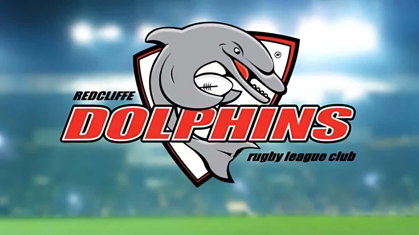 Dolphins Nrl 桌布 壁紙 — 一個卡通海豚吉祥物在盾牌標誌中抱著橄欖球，背景是模糊的體育場。