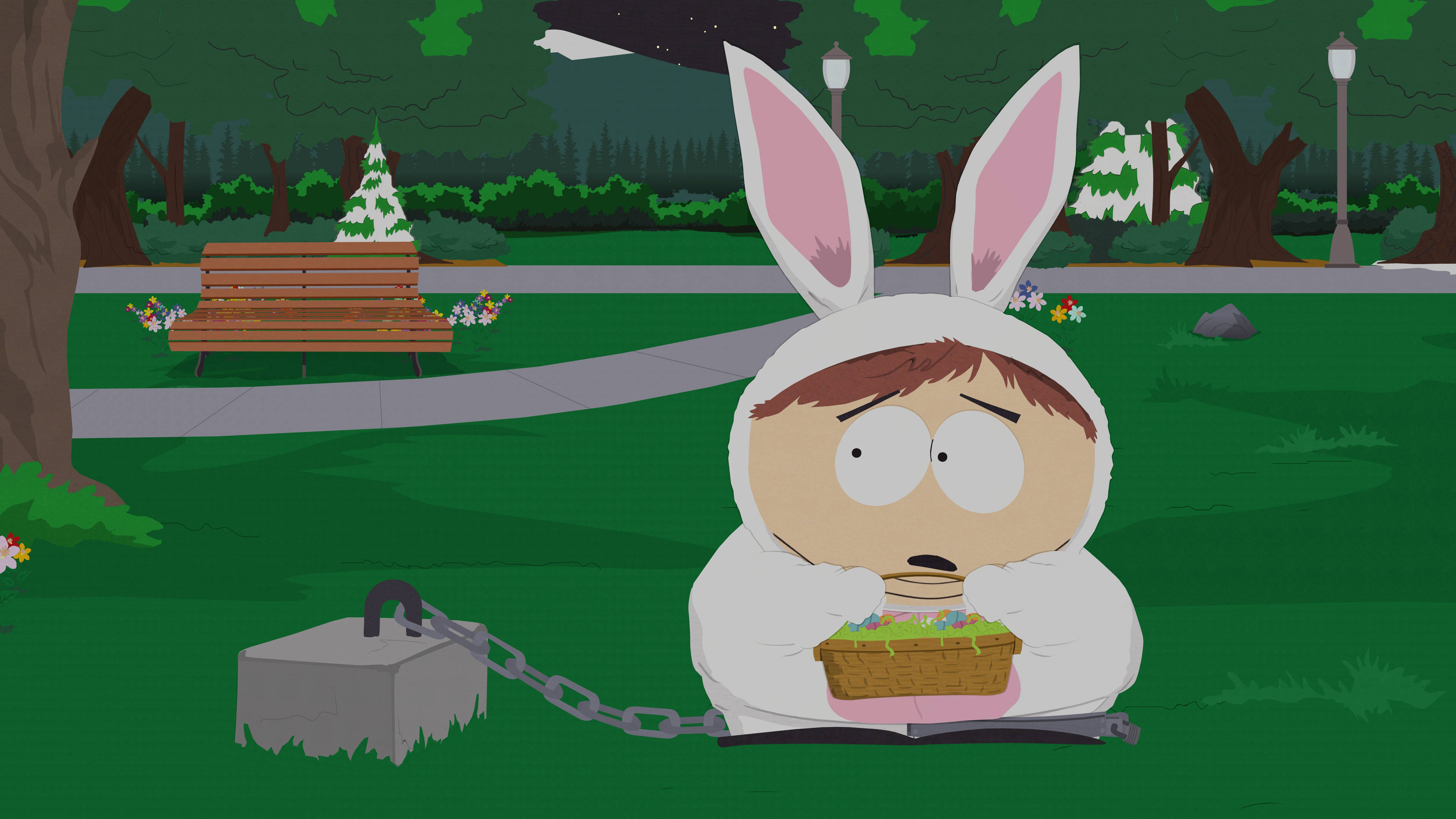 Cartman 桌布 壁紙 — 一個卡通男孩穿著兔子服裝，被鎖鏈拴在黑暗公園的石頭上，手持復活節籃子。