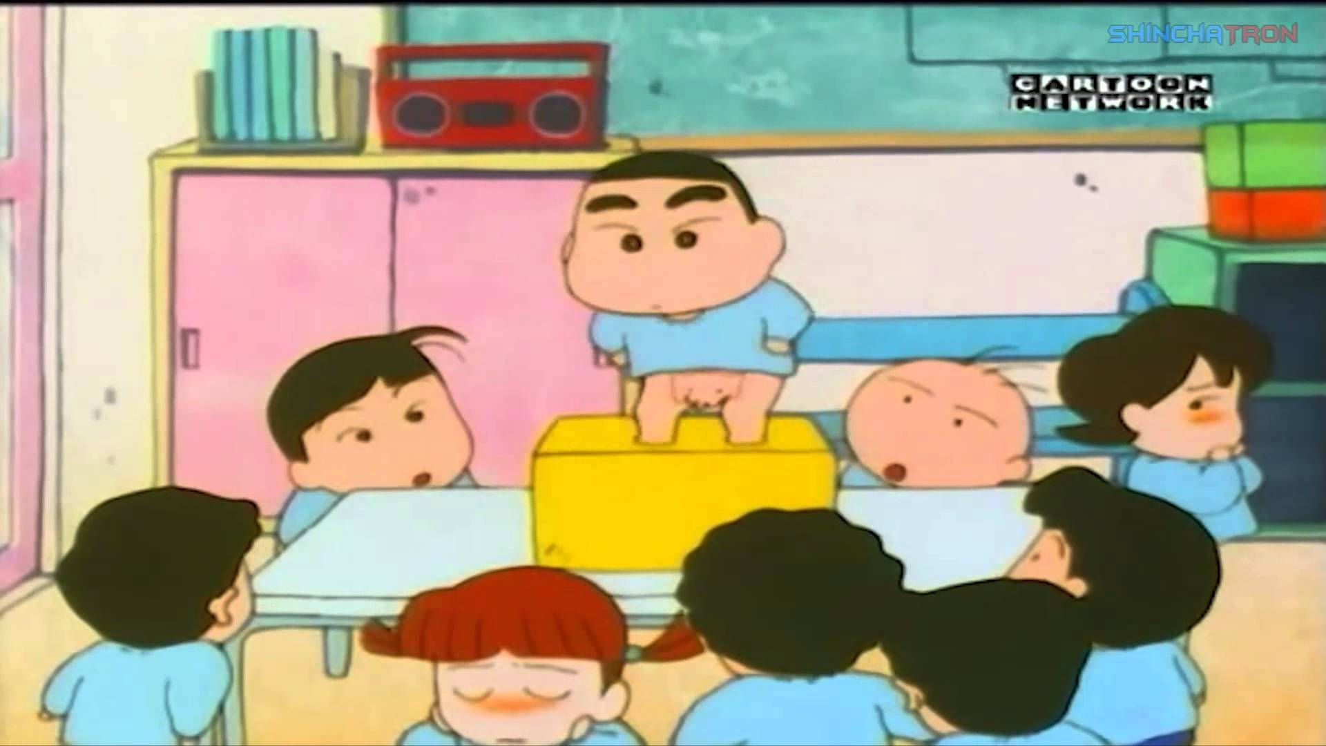 蠟筆小新 桌布 壁紙 — 一個卡通男孩站在教室裡的黃色箱子上，周圍穿著藍色制服的同學們抬頭看著他。
