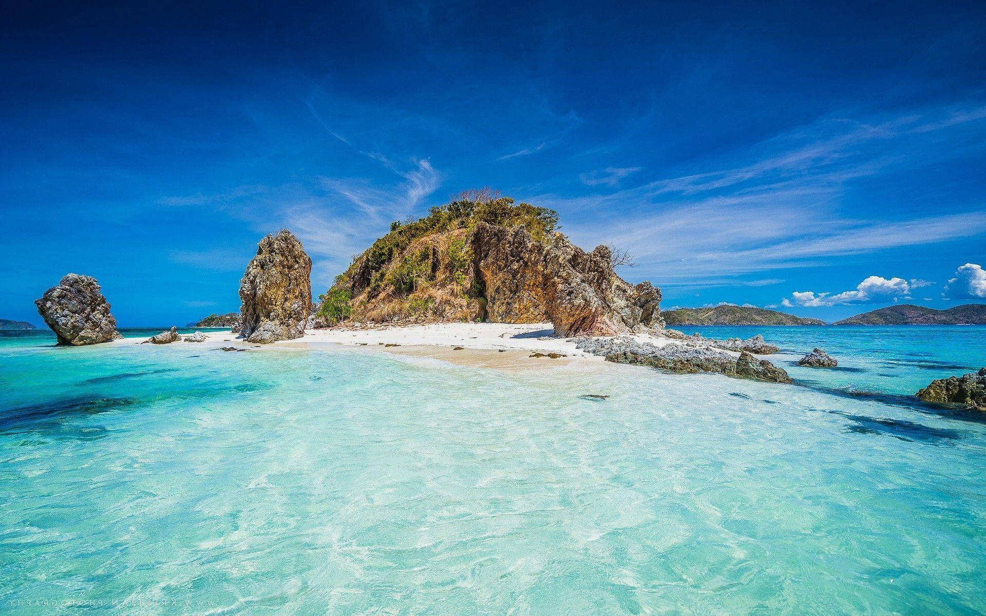 Philippines 桌布 壁紙 — 一個原始熱帶島嶼，擁有碧綠海水和白色沙灘，周圍是崎嶇的岩石地貌，在湛藍的天空下。