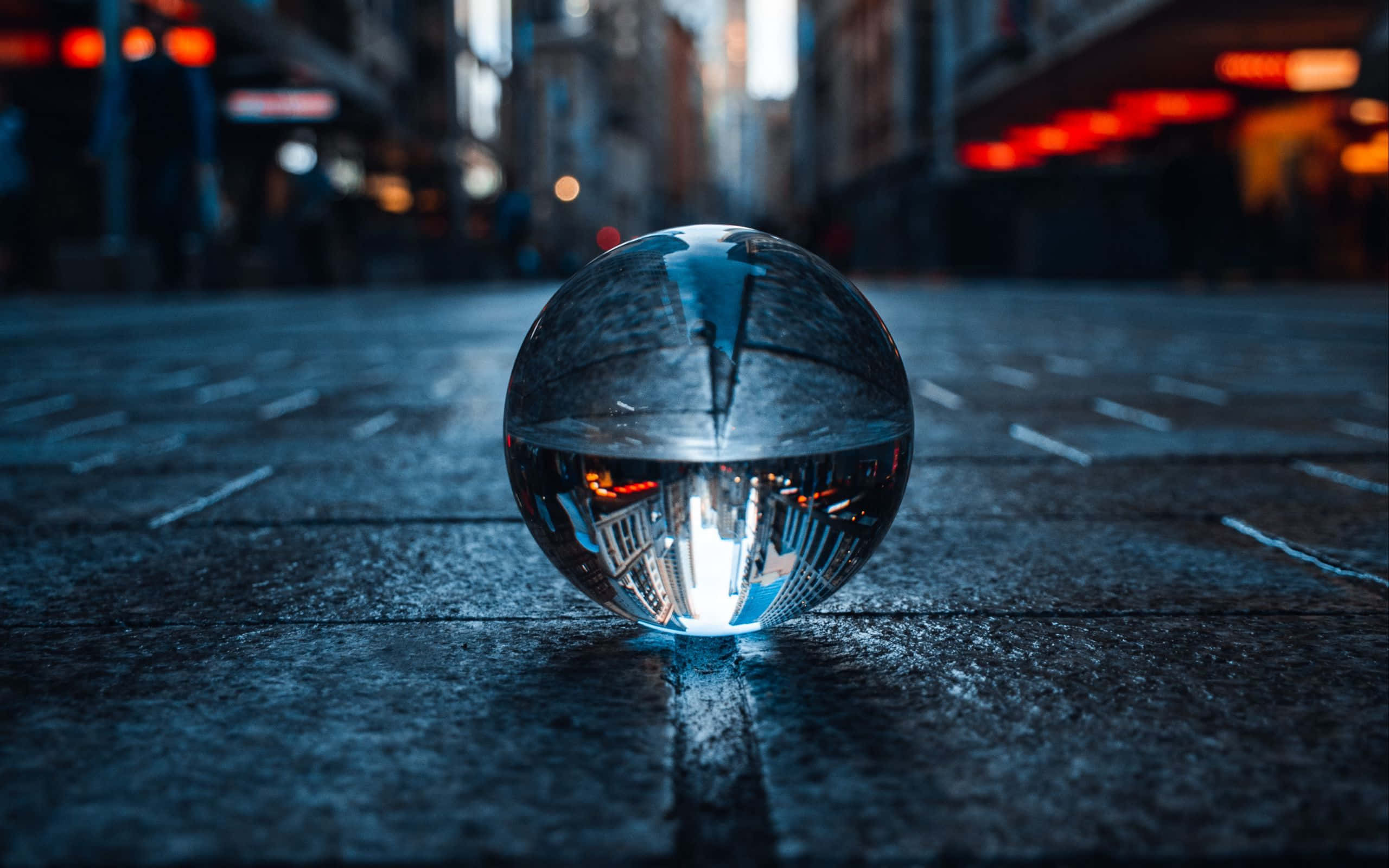 Crystal Ball 桌布 壁紙 — 一個反光玻璃球在夜晚潮濕的城市街道上，捕捉到倒置的霓虹燈光和模糊的建築物在其扭曲的表面上。