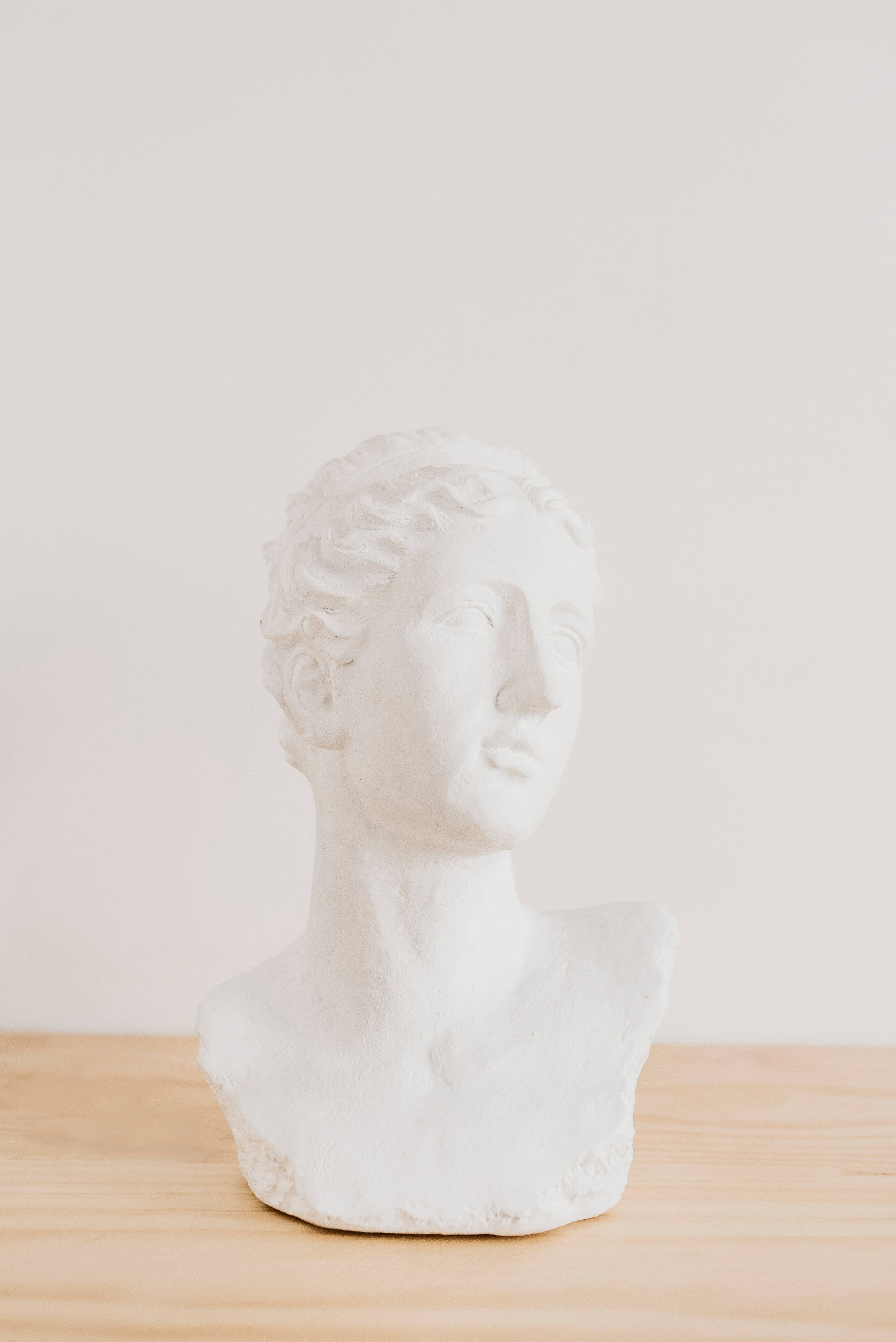 Sculpture 桌布 壁紙 — 一個古典人物的極簡白色石膏半身像放在淺色木質表面上，背景是純色米白色牆壁。