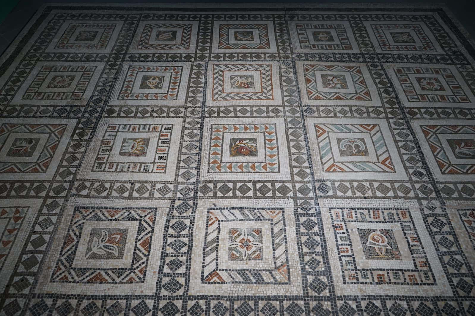 Mosaic 桌布 壁紙 — 一個古老的馬賽克地板，在昏暗燈光下呈現大地色調的幾何圖案和動物圖案。