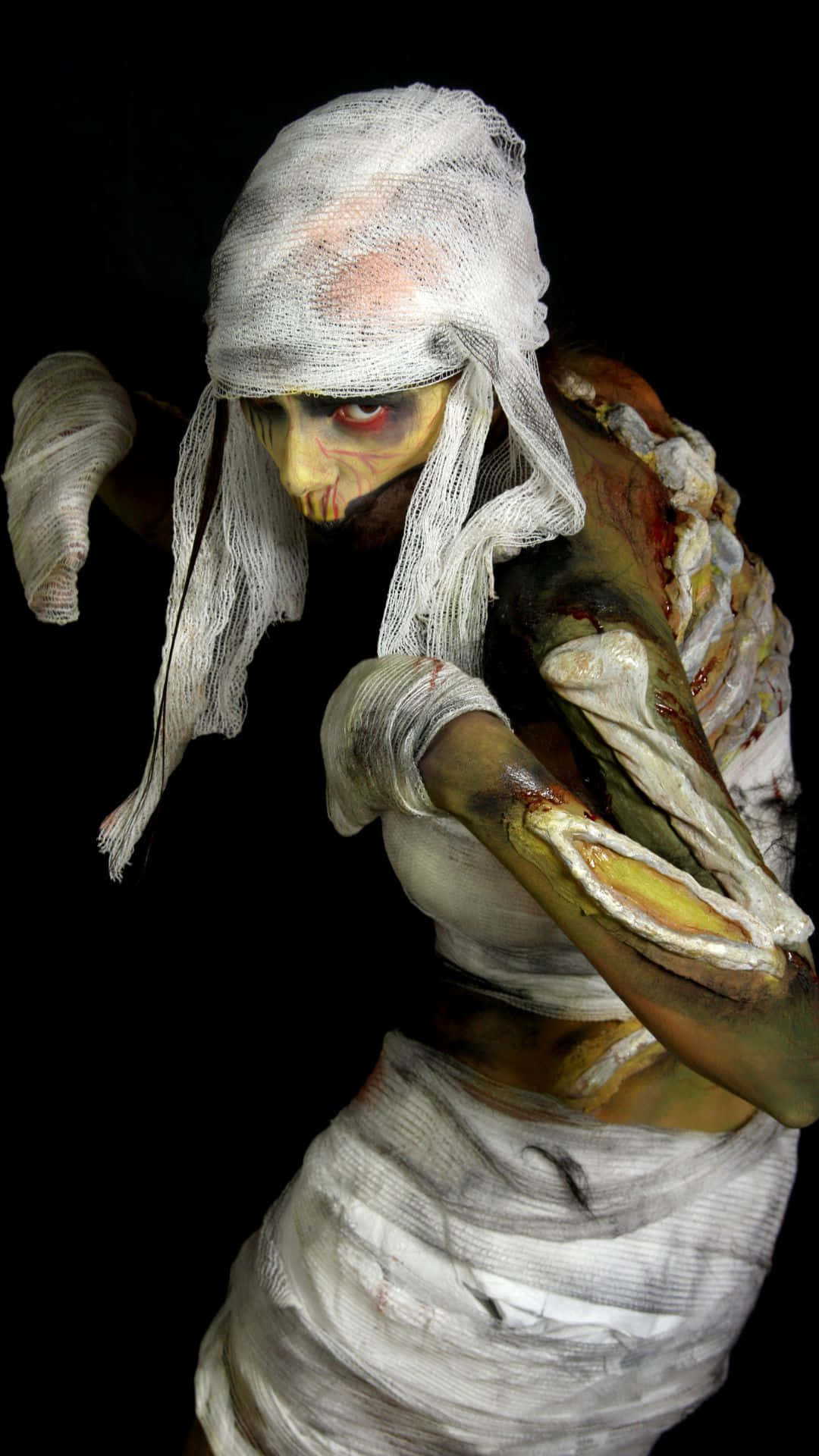 Mummy Costumes 桌布 壁紙 — 一個可怕的木乃伊，繃帶破爛，露出腐爛的肉，在黑色背景上威脅地凝視著。