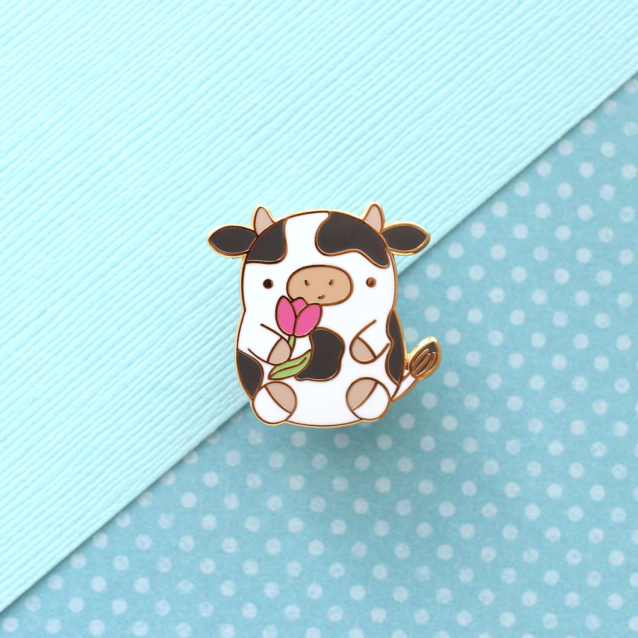 Kawaii Cow 桌布 壁紙 — 一個可愛的卡通牛琺瑯別針拿著粉紅色鬱金香，放在淺藍色紋理紙上，帶有白色圓點。