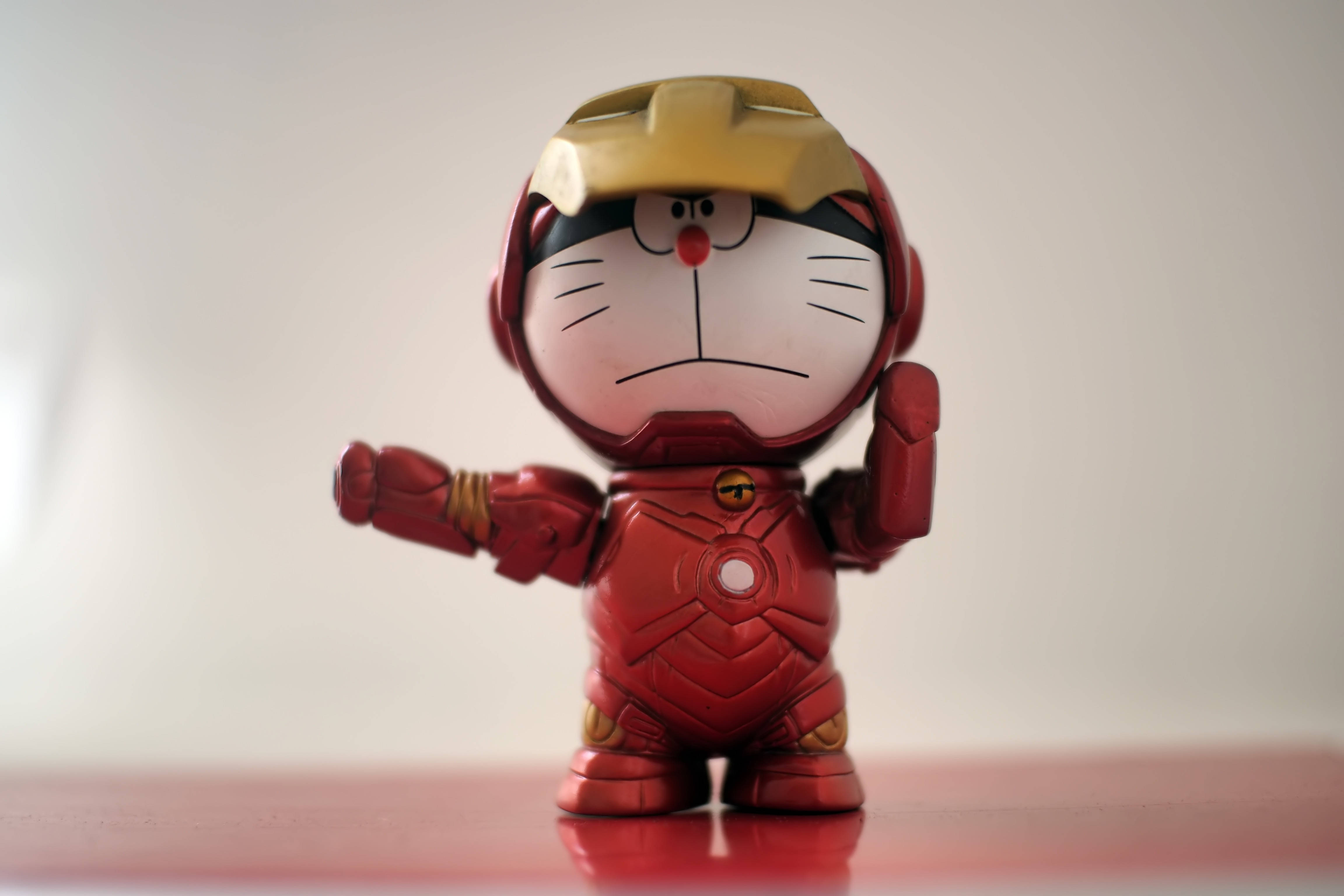 Doraemon 桌布 壁紙 — 一個可愛的哆啦A夢公仔穿著精細的紅色和金色鋼鐵人套裝，自信地站在反光表面上。