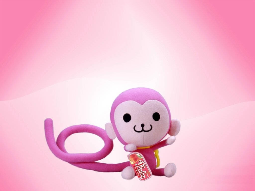 Baby Monkey 桌布 壁紙 — 一個可愛的粉紅色毛絨猴子玩具，帶有長長的捲曲尾巴，坐在柔和的漸變粉紅色背景前。