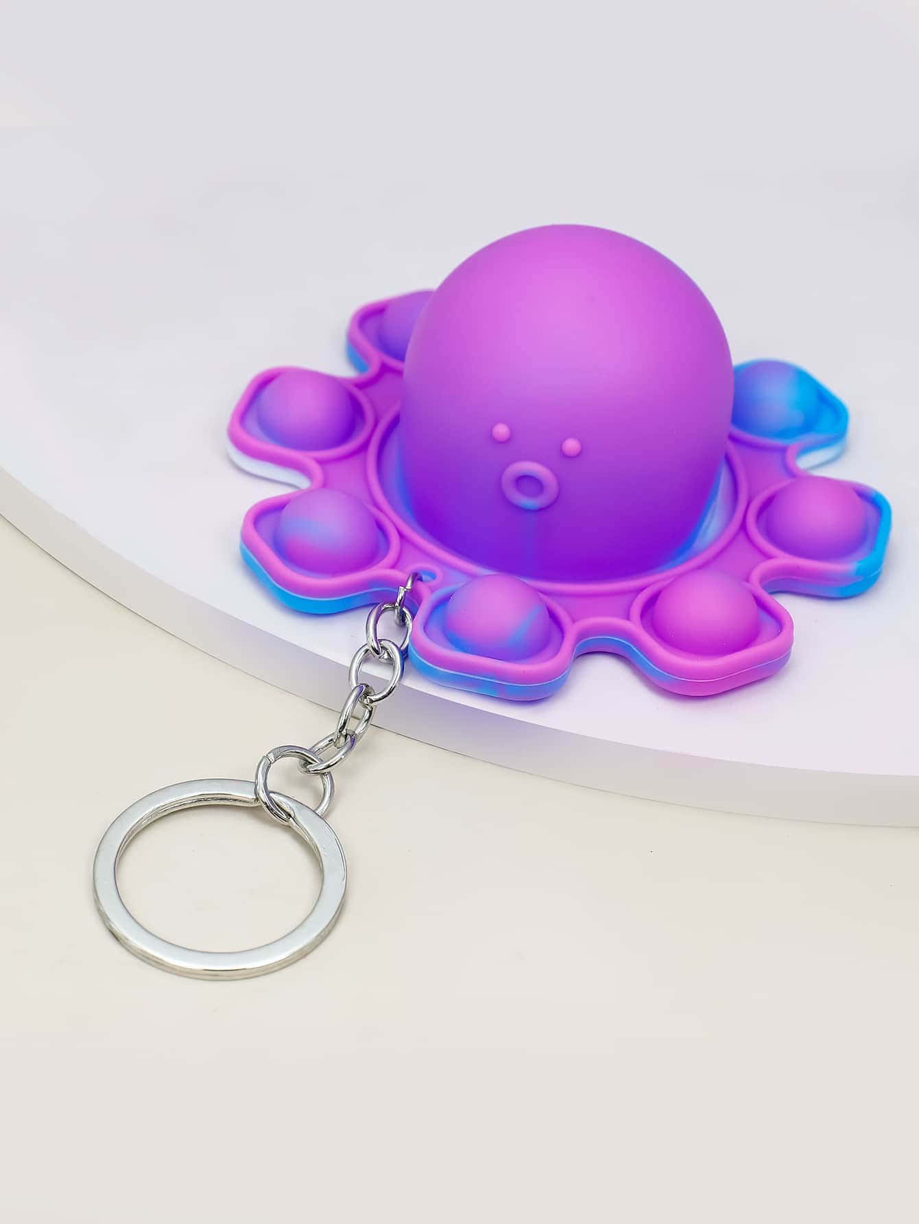 Popit 桌布 壁紙 — 一個可愛的紫色和藍色章魚形減壓玩具，帶有金屬鑰匙圈，放置在白色表面上。