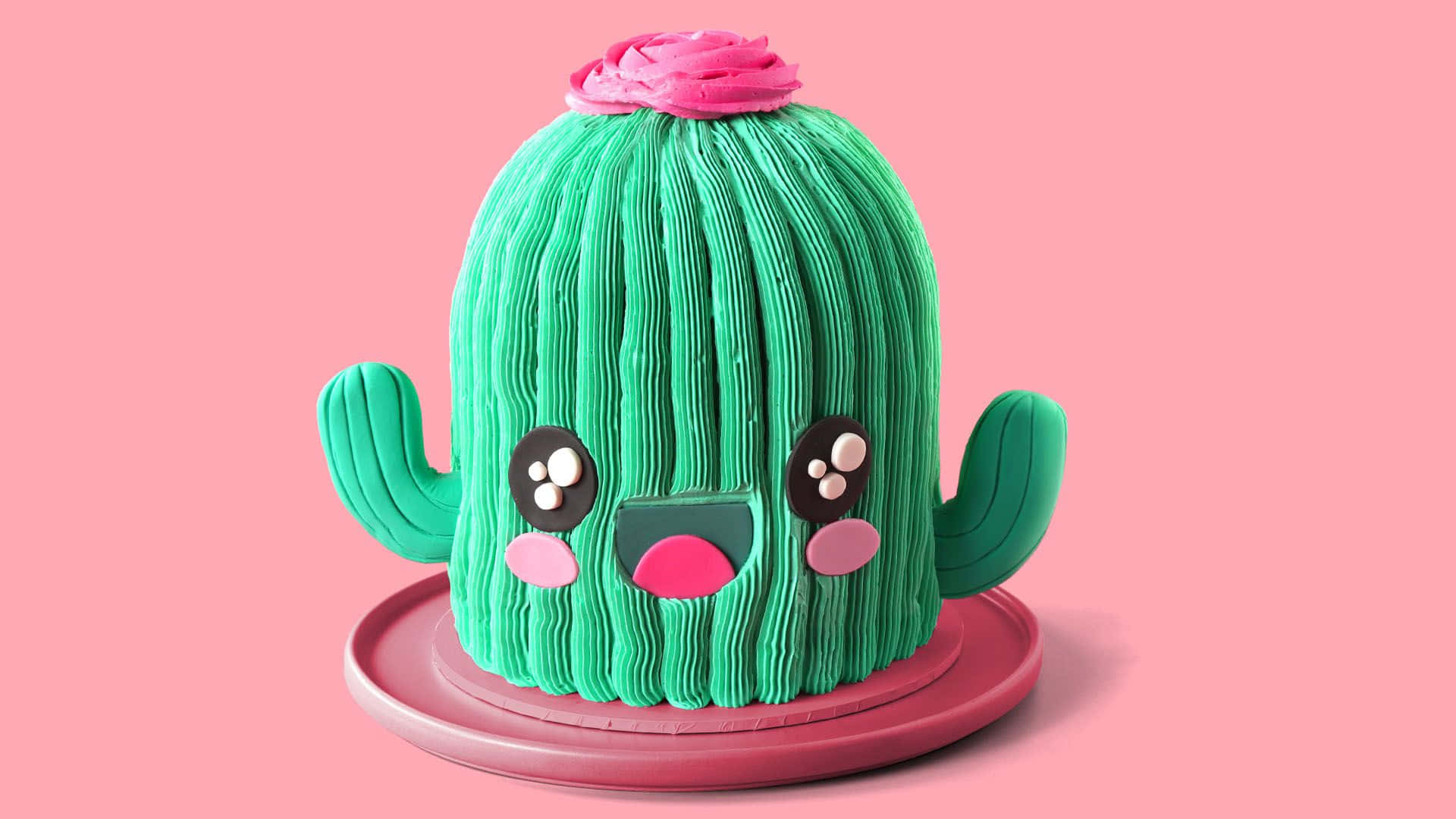 Kawaii Cactus 桌布 壁紙 — 一個可愛的綠色仙人掌蛋糕，帶有粉紅色糖霜和大眼睛，放在粉紅色盤子上，背景是柔和的粉紅色。