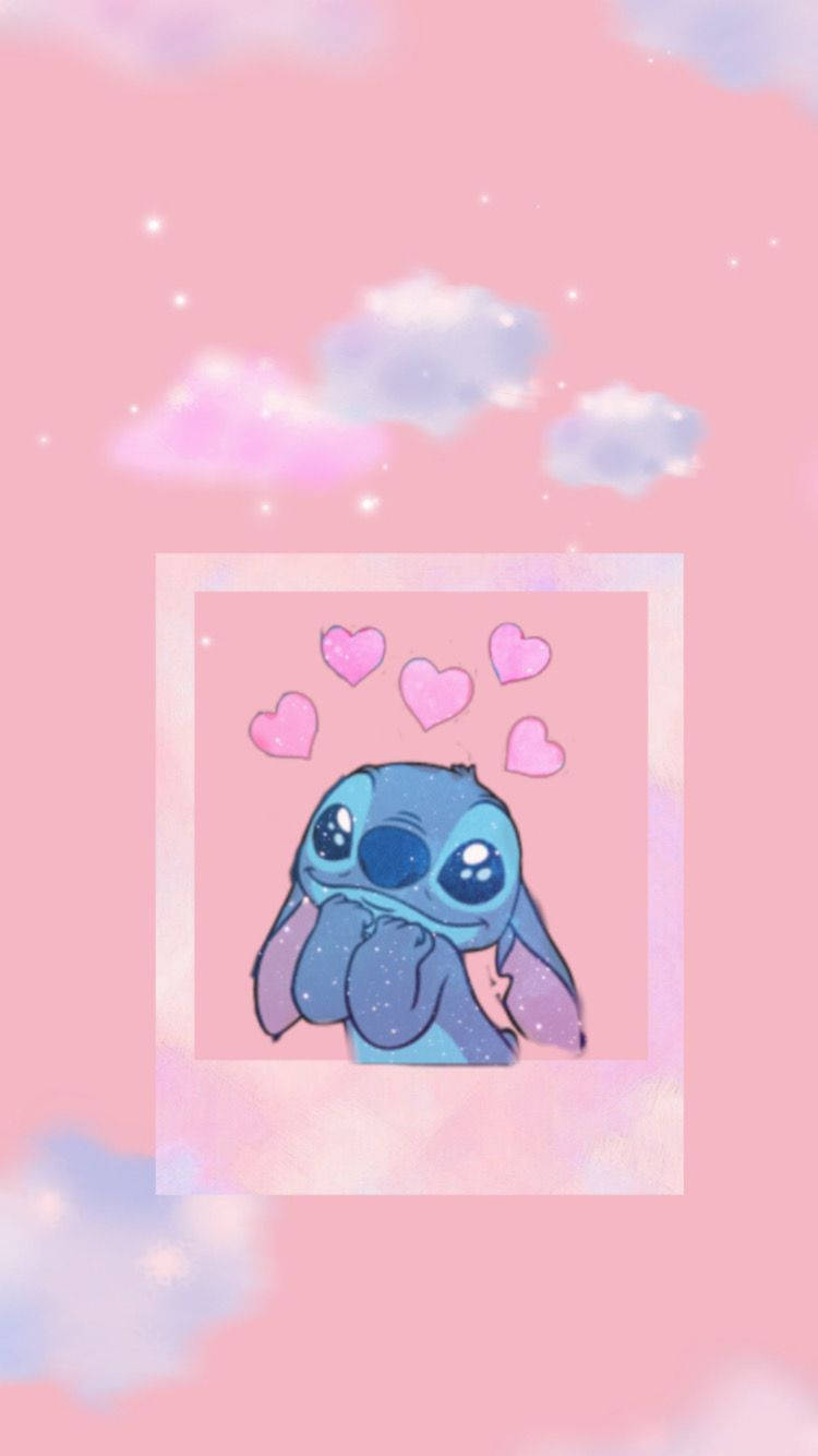 cute stitch iPhone 桌布 壁紙 — 一個可愛的藍色外星人，有大眼睛和漂浮的粉紅色愛心，背景是柔和的粉紅色天空和蓬鬆的雲朵。