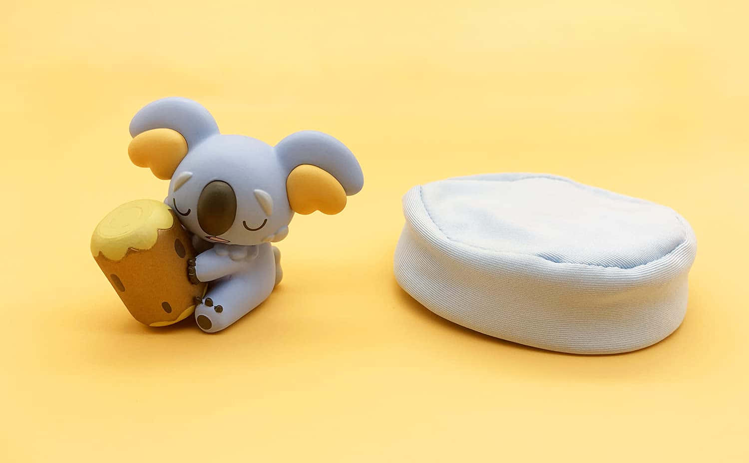 Sleeping 桌布 壁紙 — 一個可愛的藍色無尾熊公仔在溫暖的黃色背景上抱著一個蜂蜜罐，旁邊有一個淺藍色的布袋。