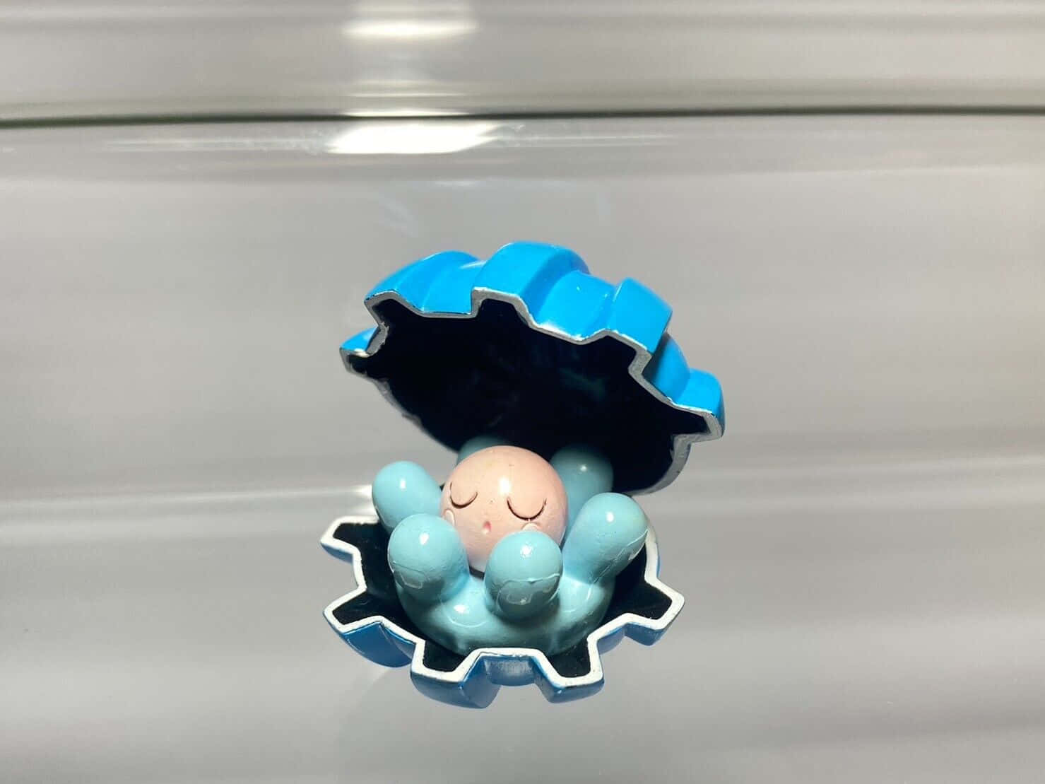 藍色 桌布 壁紙 — 一個可愛的藍色貝殼公仔，裡面有一顆睡著的粉紅色珍珠，放在反光的銀色表面上。