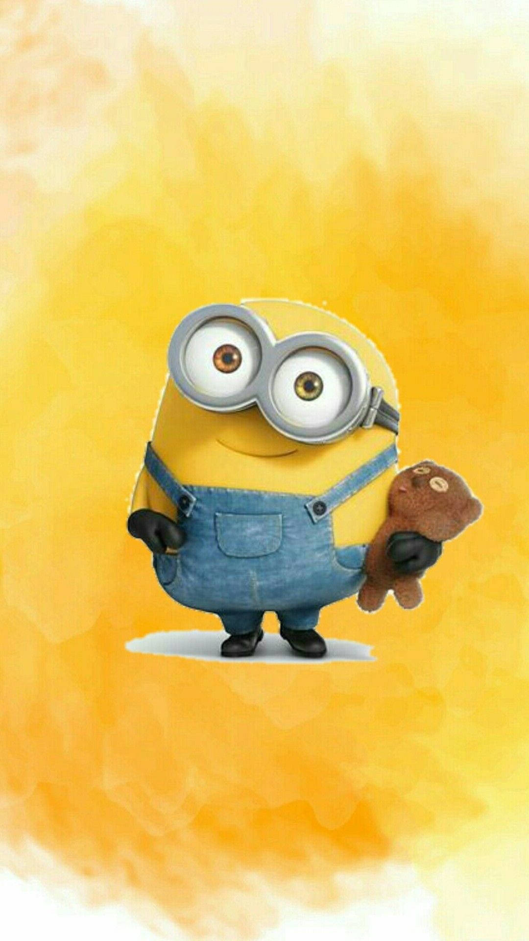 Minion Phone 桌布 壁紙 — 一個可愛的黃色小小兵穿著藍色吊帶褲，在溫暖的黃色水彩背景前抱著一隻棕色泰迪熊。